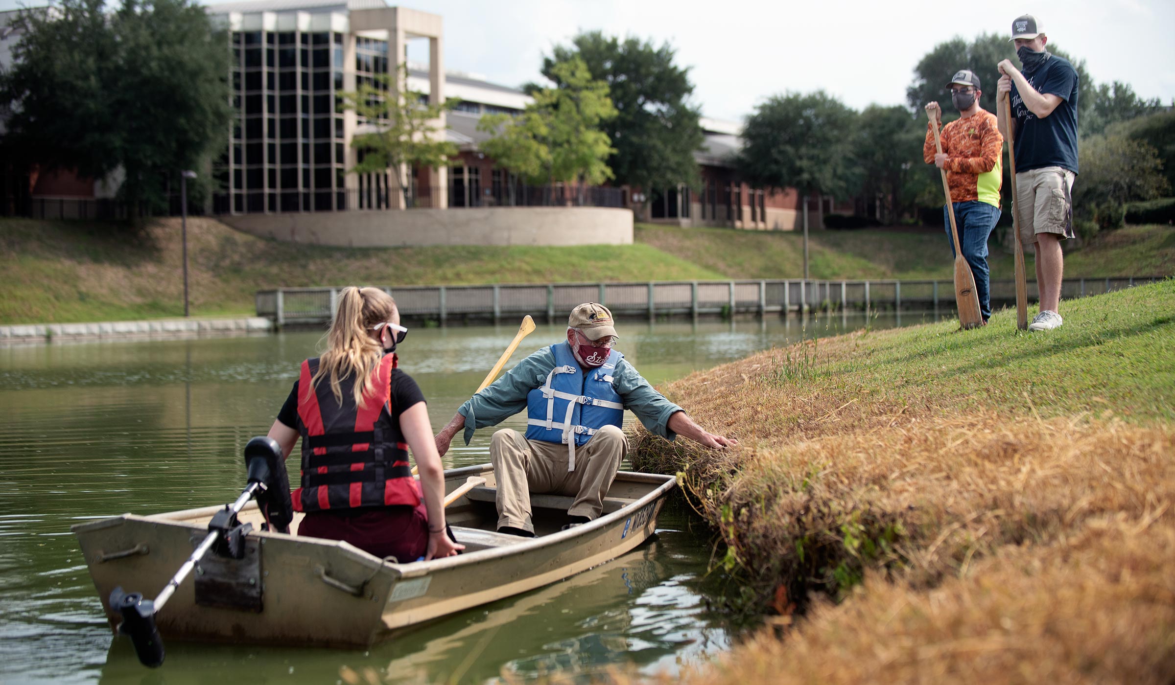 With Sanderson in the background, A professor and student push off from the Chadwick Lake grassy shore, while two other students look on.