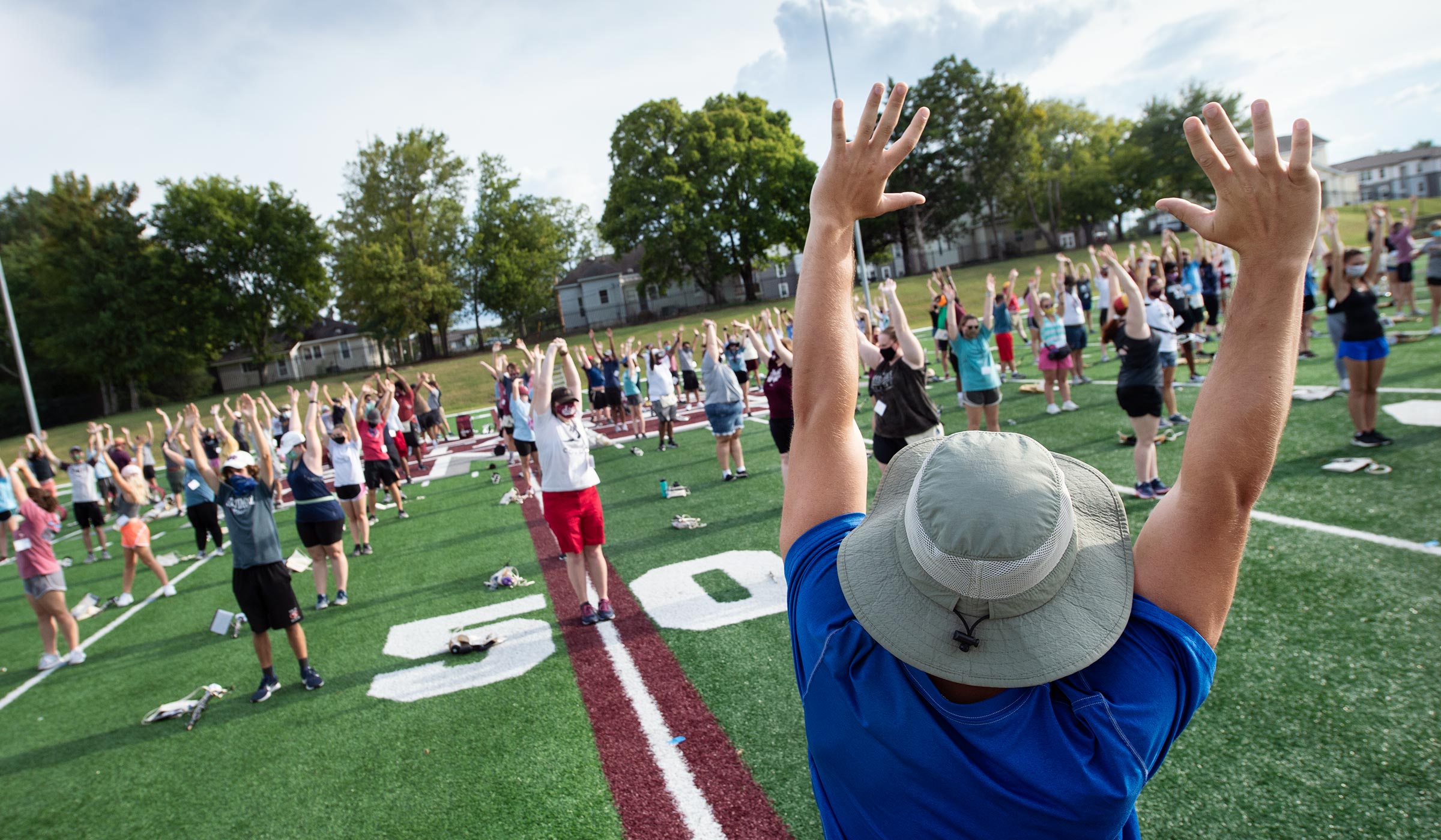 Drum Major stretches his arms overhead, leading the band in a warm-up on their practice fields.