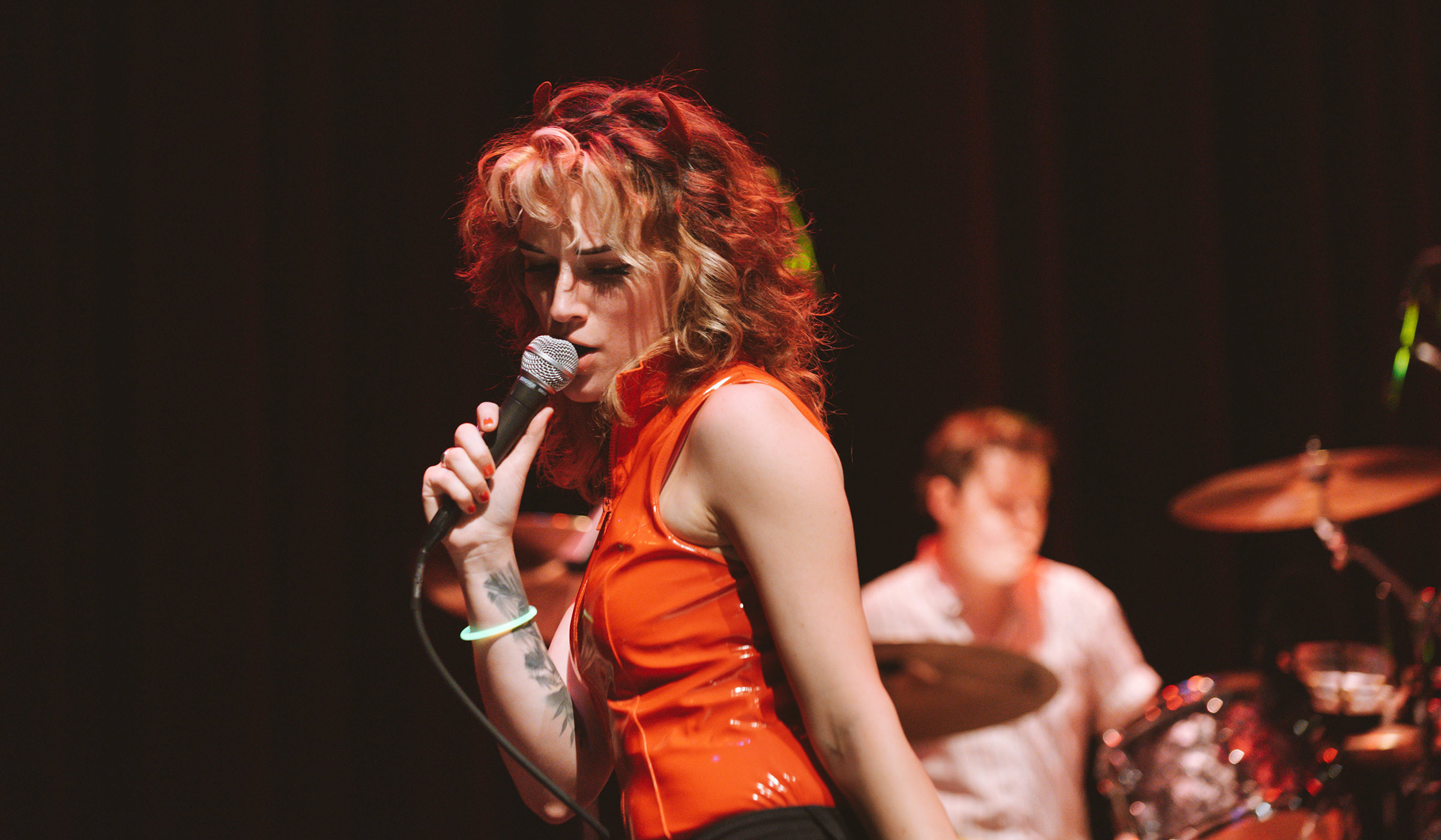 The lead singer of the rock band Flight Attendant sings into a mike on the Bettersworth stage, with band's drummer behind her.