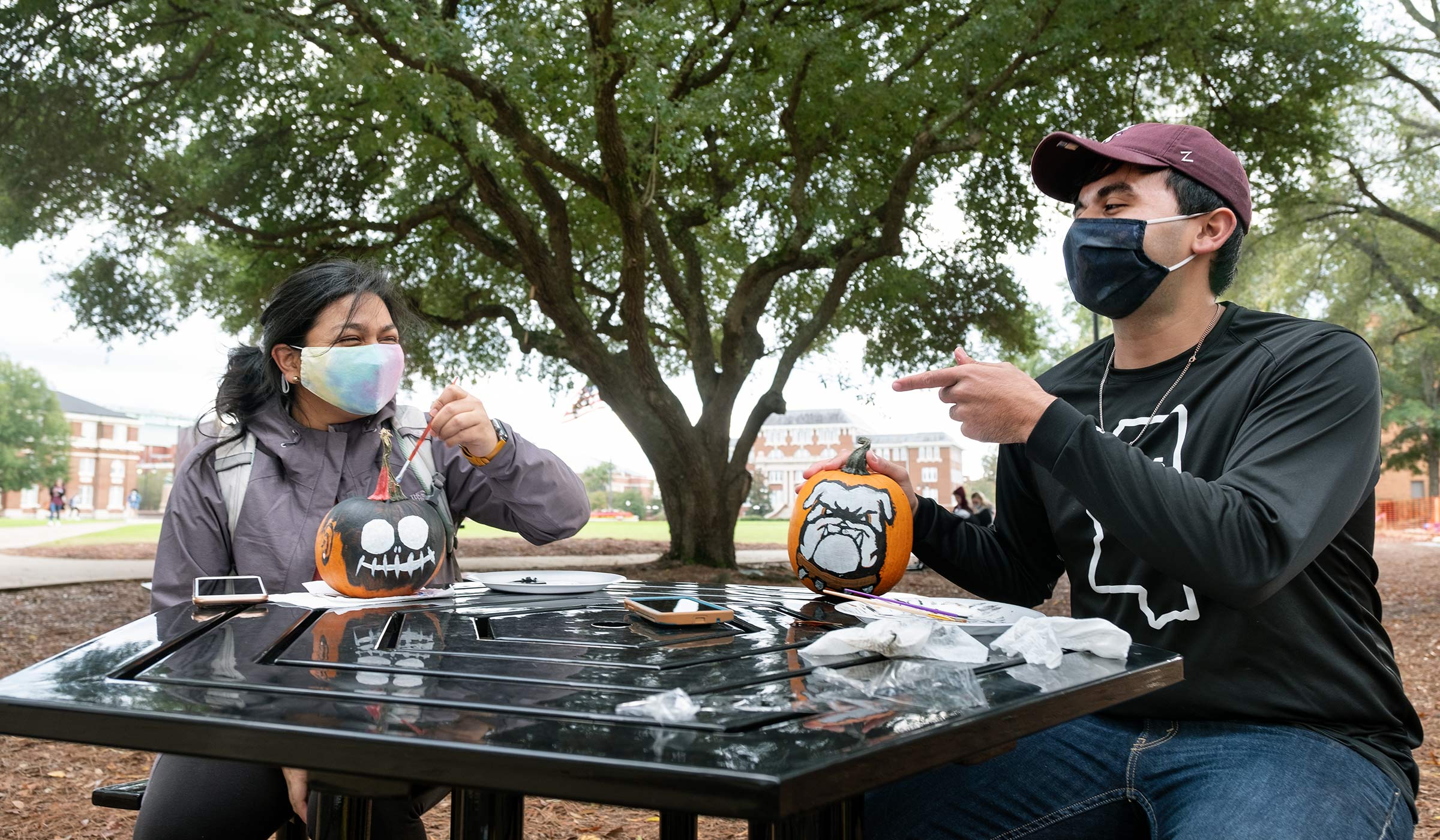 Two students paint Halloween pumpkins at one of the picnic tables placed in the Drill Field near Colvard Union.
