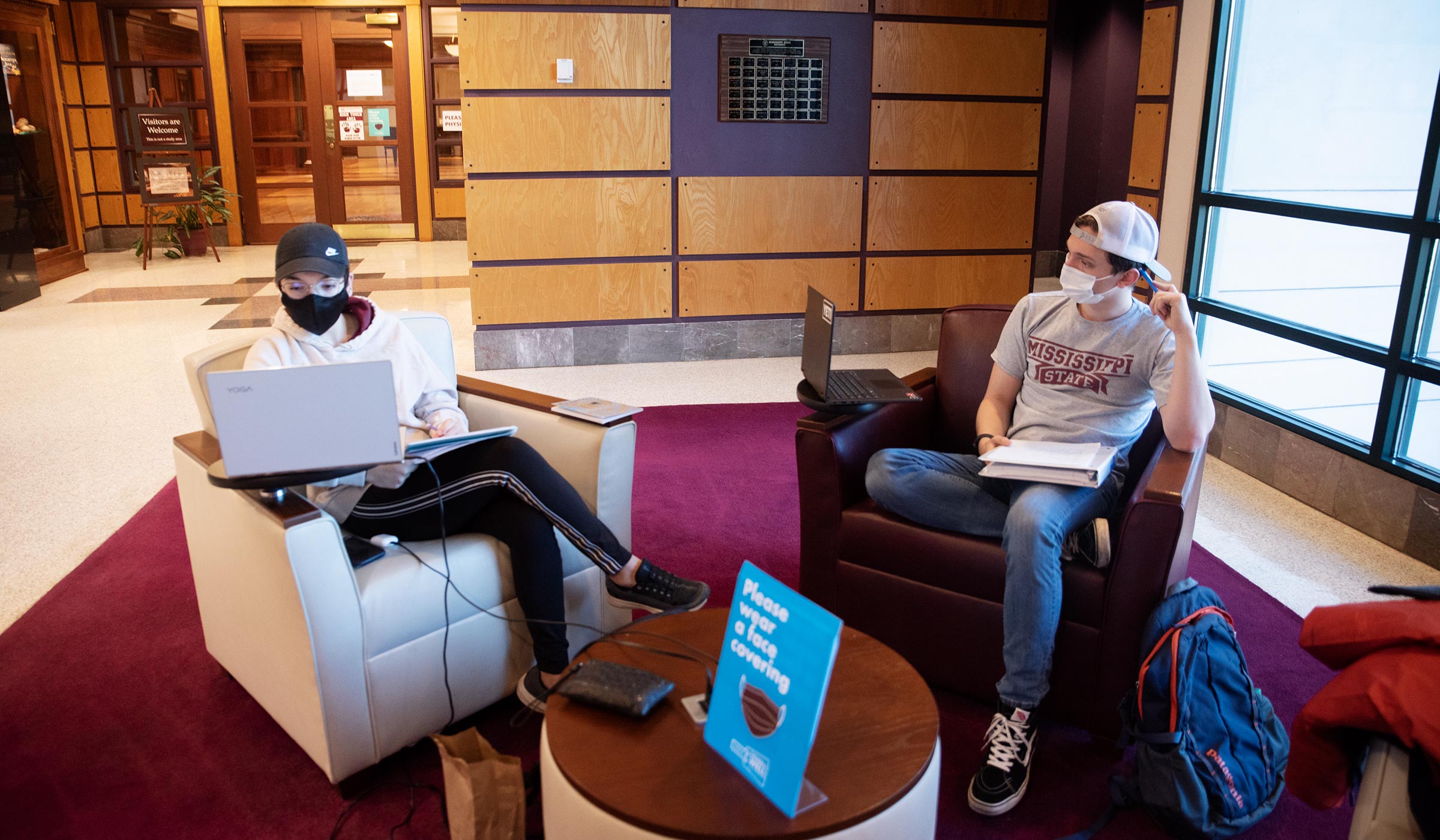Two students wearing Covid masks study in leather armchairs in Mitchell Memorial Library.