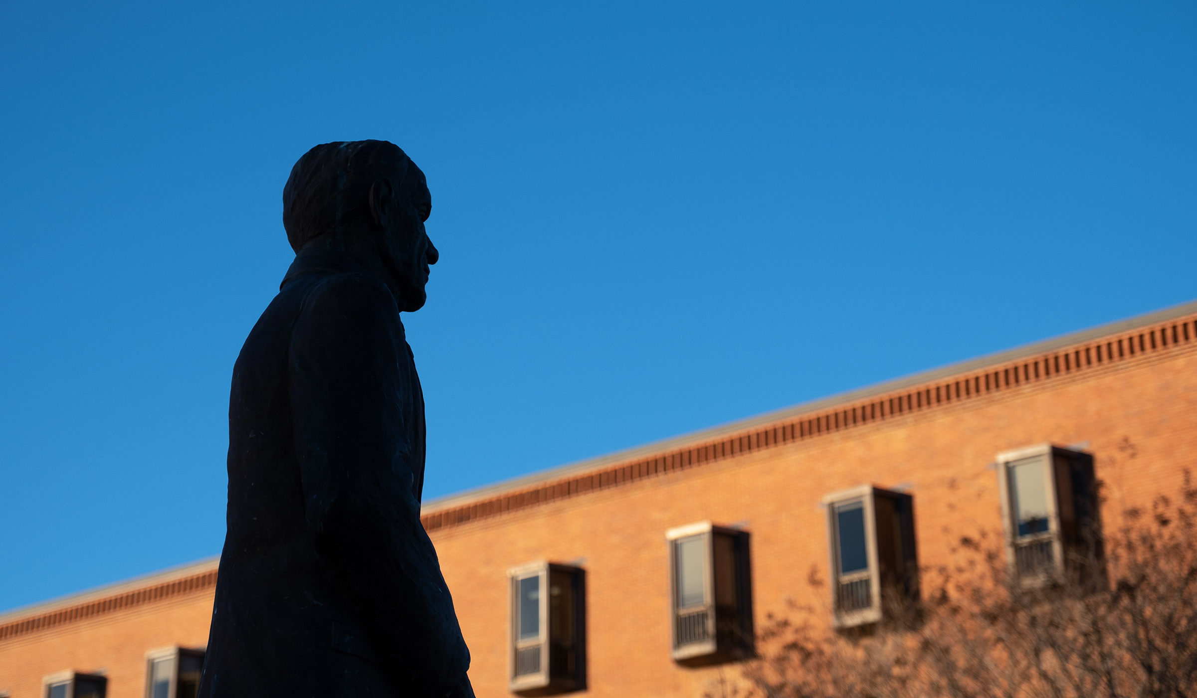 The Sonny Montgomery statue stands in silhouette with blue sky and McCool beyond.