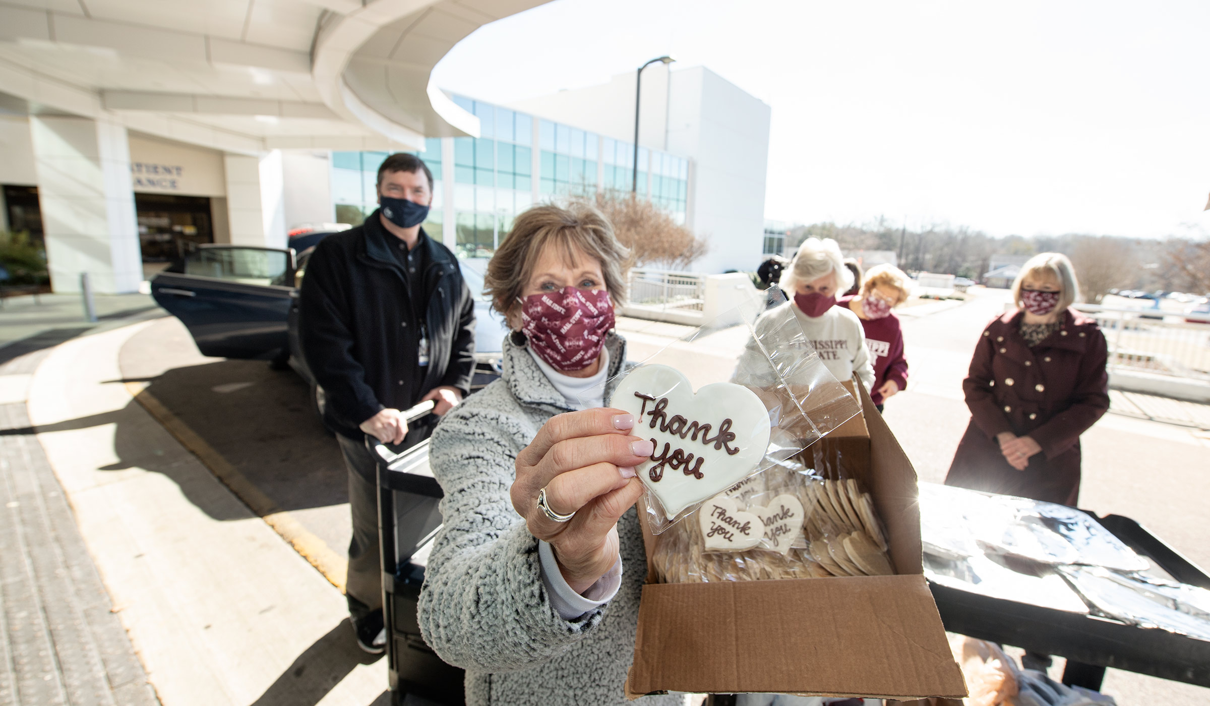 MSU Alumni Carol Reed holds a &quot;Thank You&quot; cookie up at Oktibbeha County Hospital, as fellow Okitbbeha County Alumni ready food to go in to hospital staff treating Covid patients.