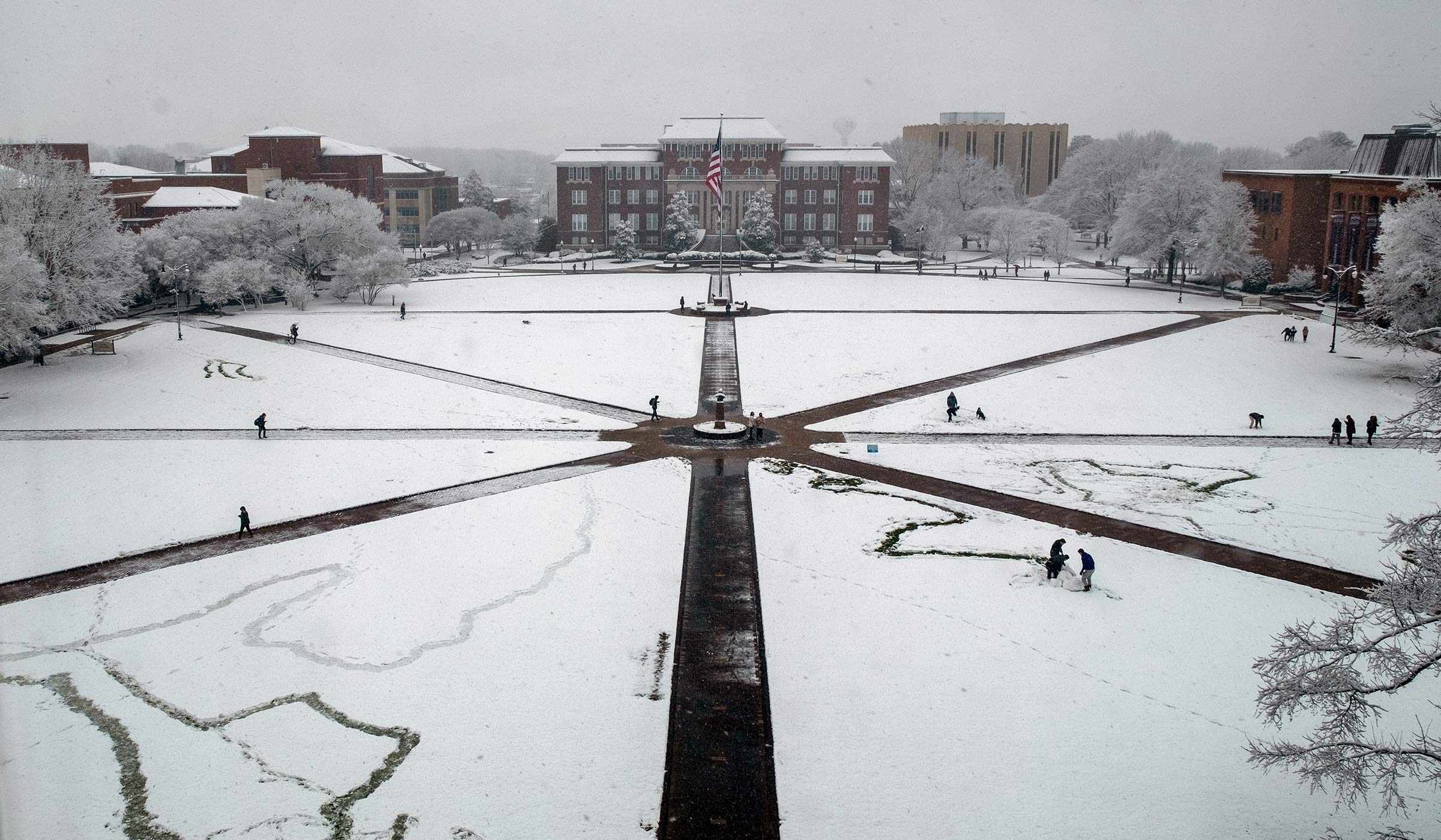 View looking down on a snow-covered Drill Field with students walking and making snowmen.