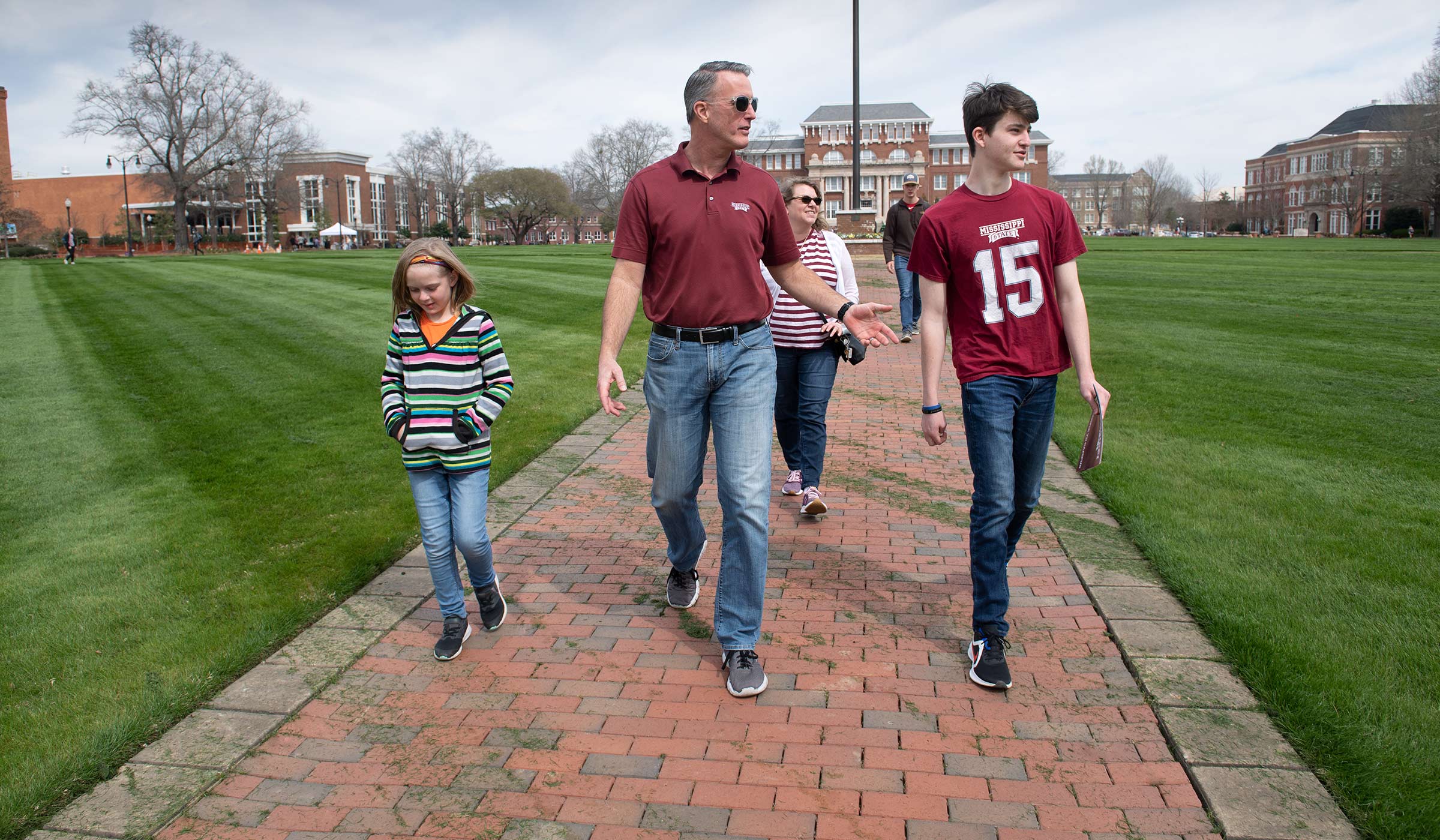 Surrounded by the freshly mown grass of the Drill Field, the Brooks family walks down the central sidewalk, pointing out the sights to their two children.