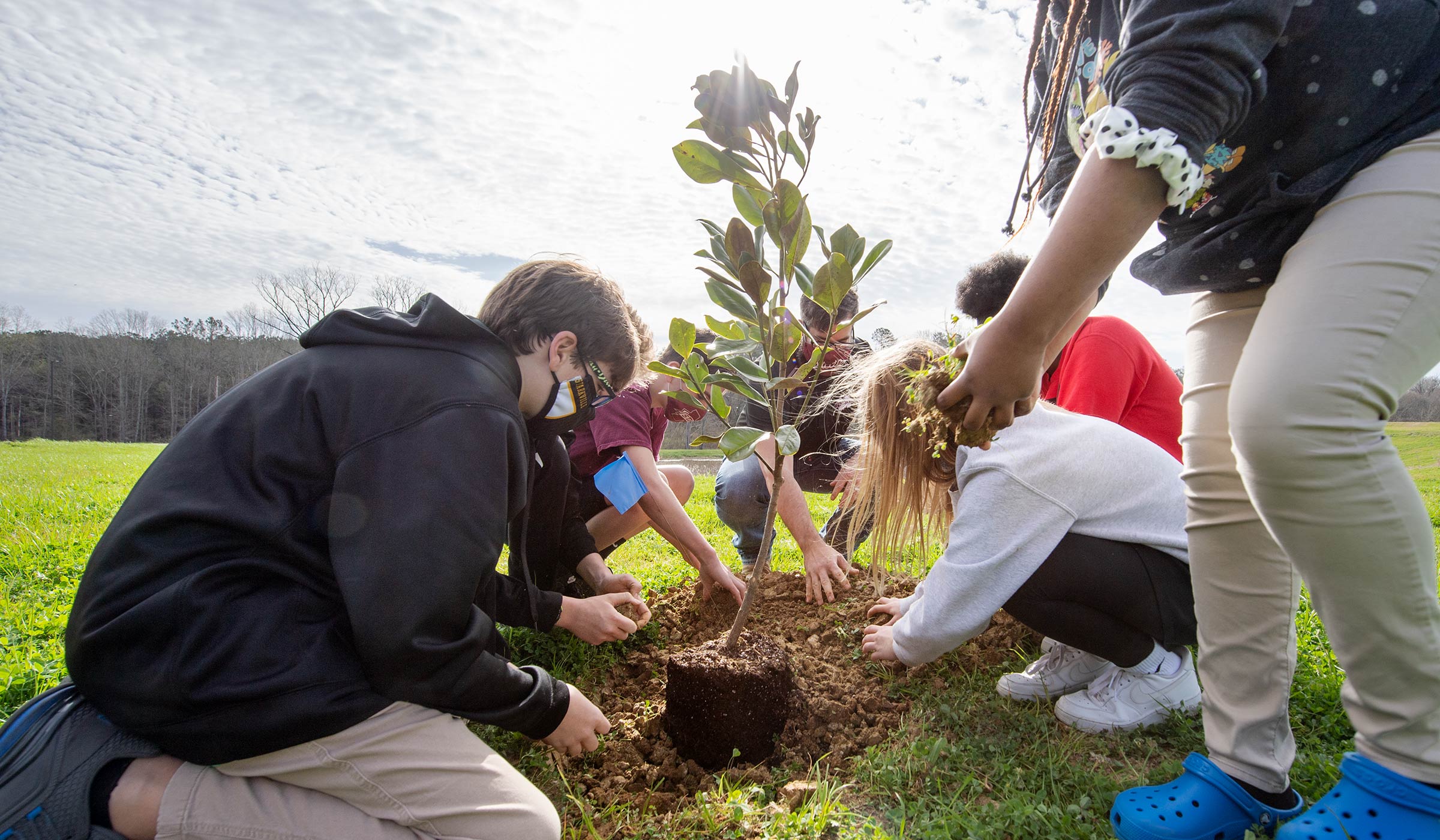 Partnership Middle School students scoop handfuls of dirt onto a freshly planted tree.