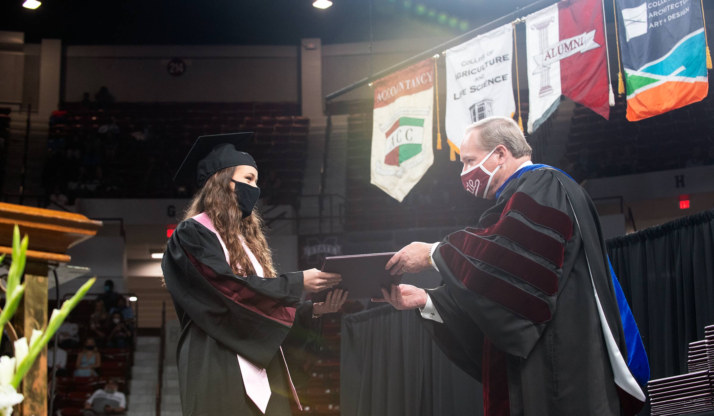 Female in black and maroon graduation regalia accepting diploma from man in doctoral robes
