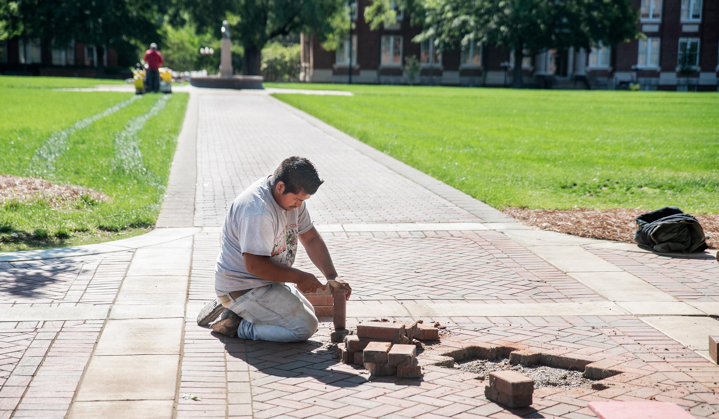 A worker lays bricks on a Drill Field sidewalk.