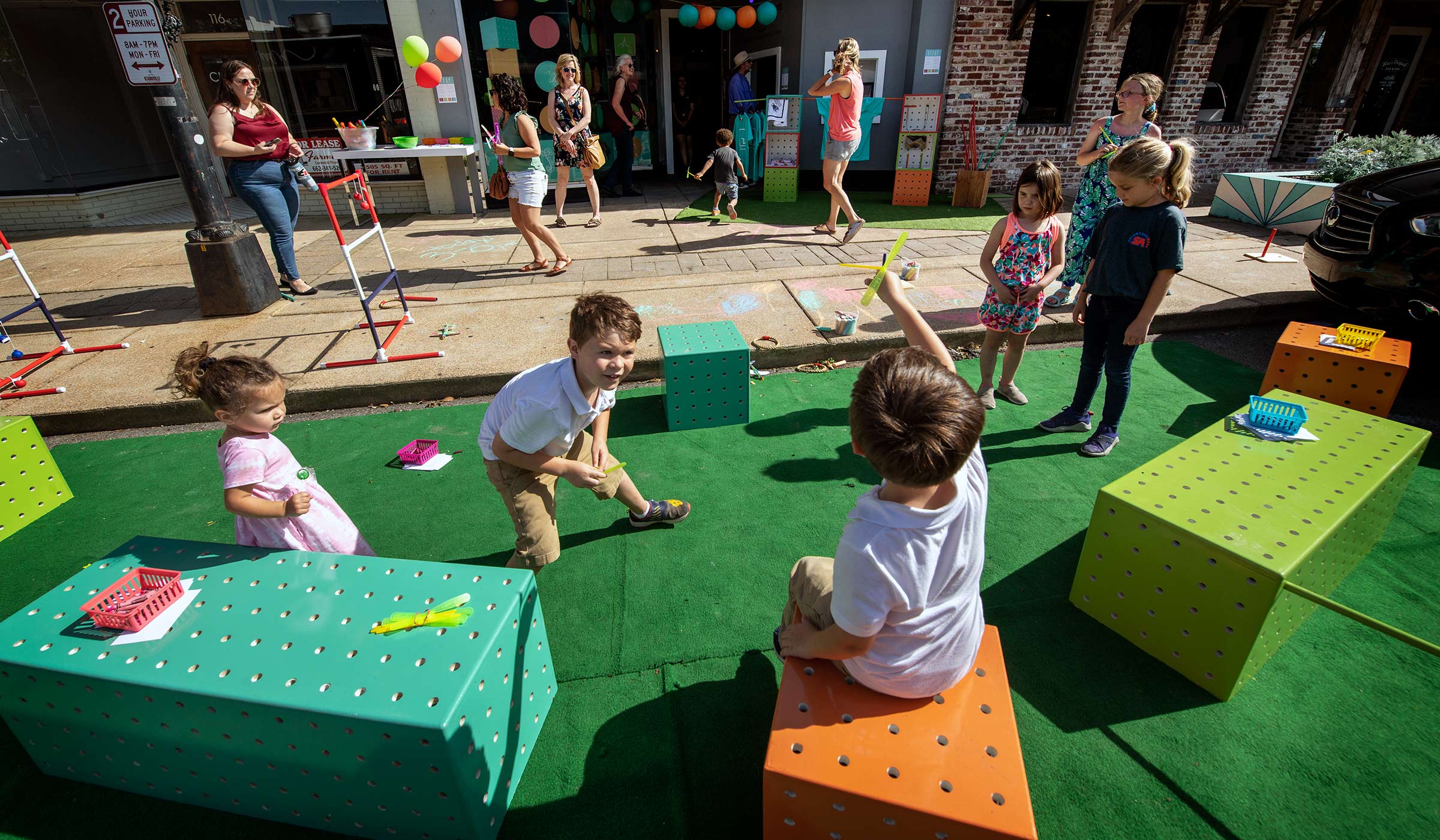 Children play and sit on colorful SITSY modules placed on astroturf outside The Idea Shop in downtown Starkville.