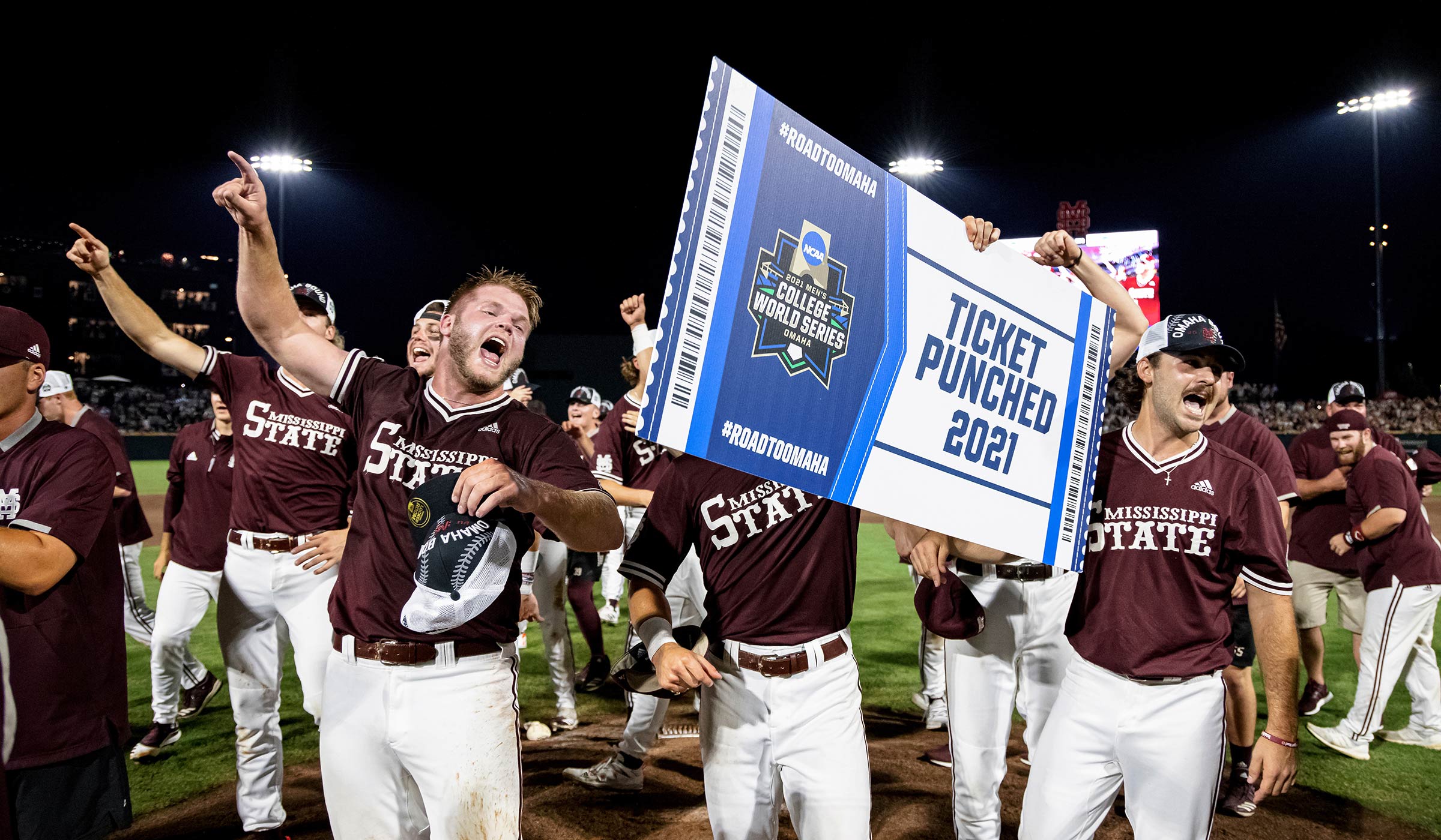 Baseball players in maroon jerseys and white pants celebrating on field with signs