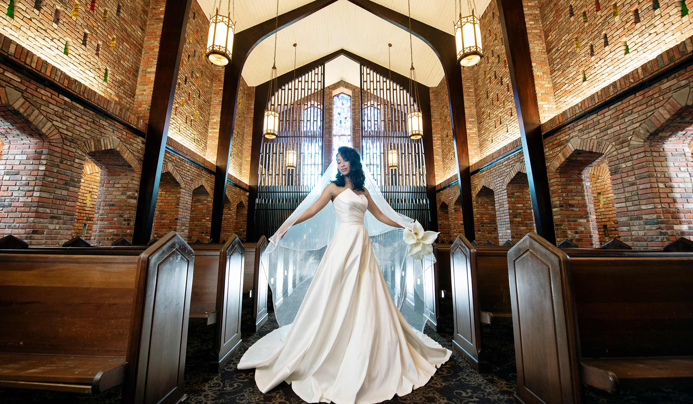Bride in white gown twirling in wooden and brick chapel with stained glass in background