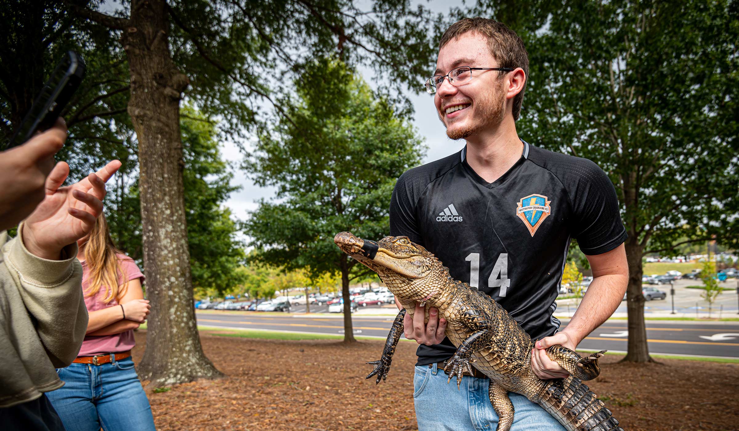Guy with glasses in dark shirt holding young alligator
