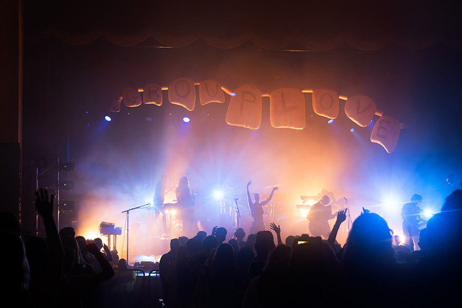 Band on stage with yellow and blue lights glowing around them with audience in foreground