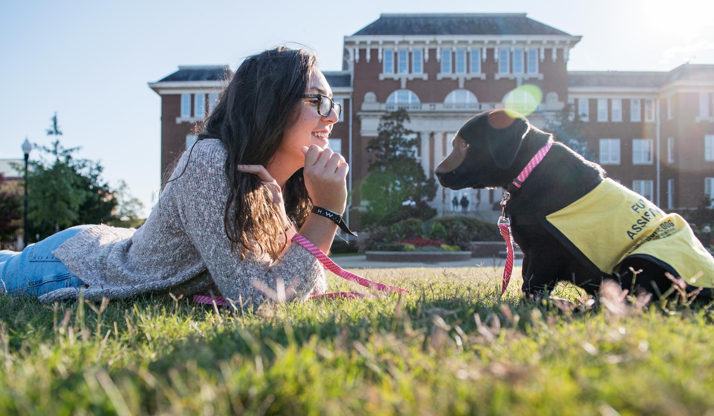 Maya Harlow lays down next to a service dog on the MSU Drill Field