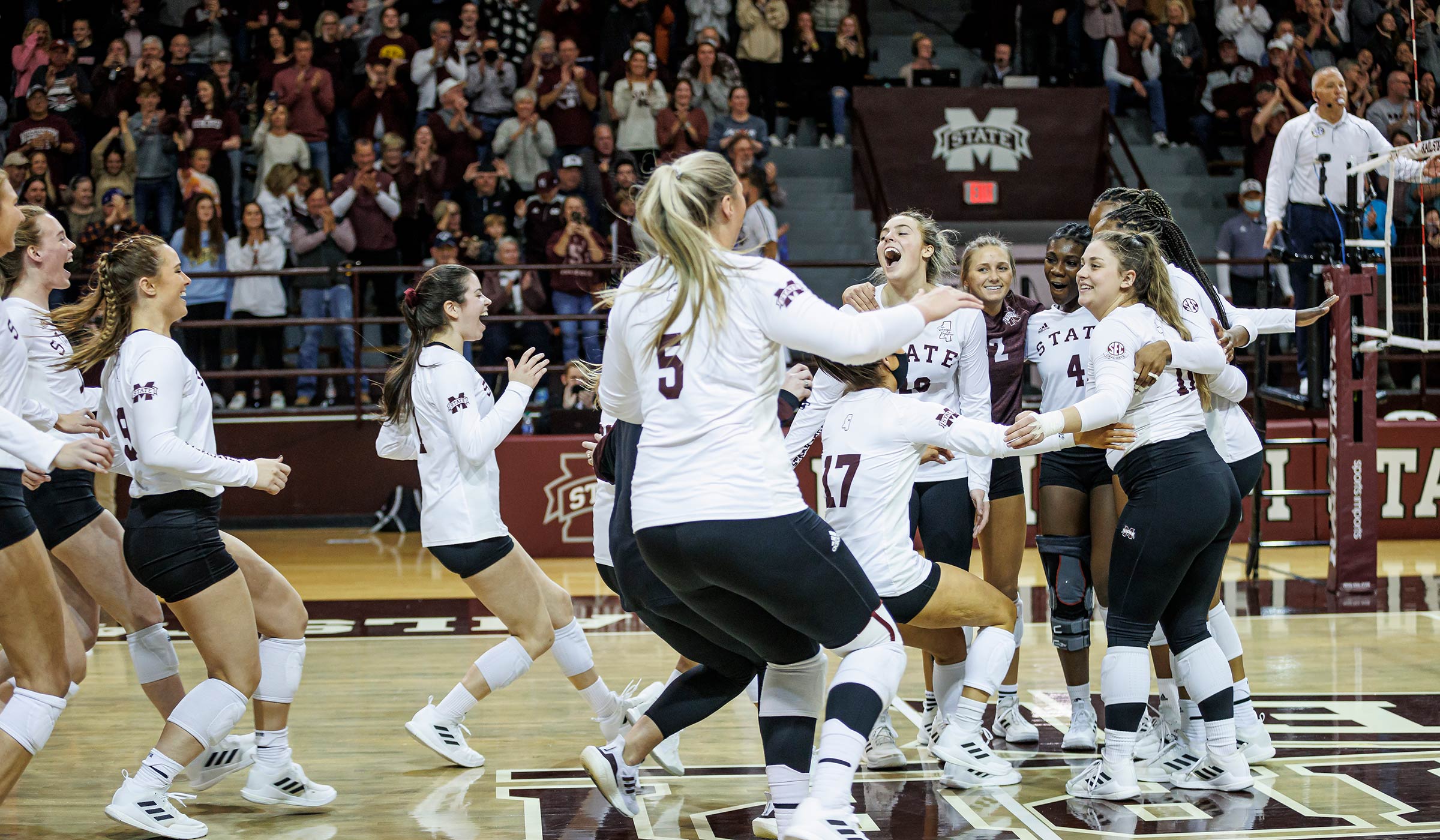 Girls in white shirts and black shorts running towards team mate to celebrate in front of crowd