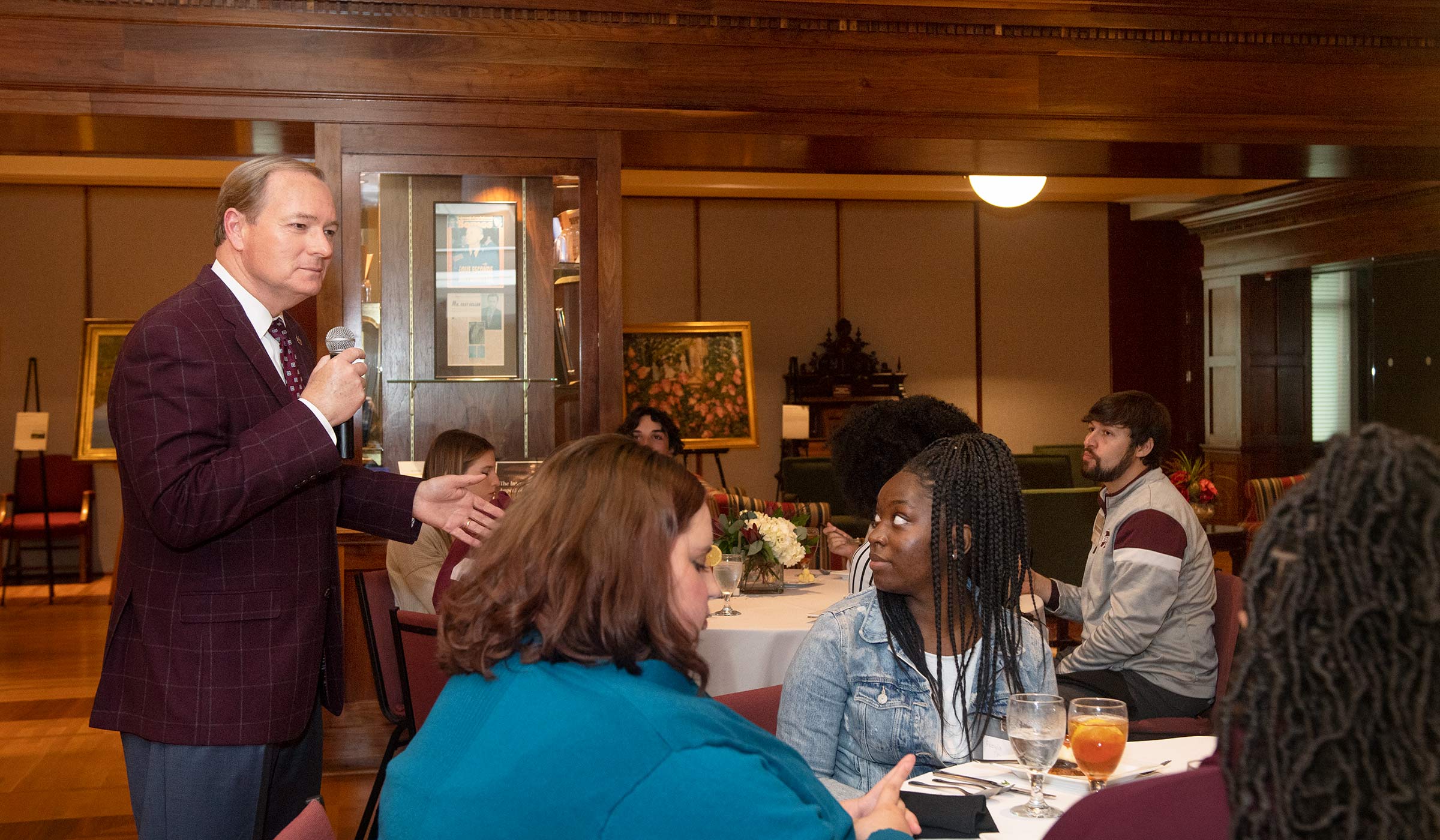 Man in maroon blazer speaking to students at tables