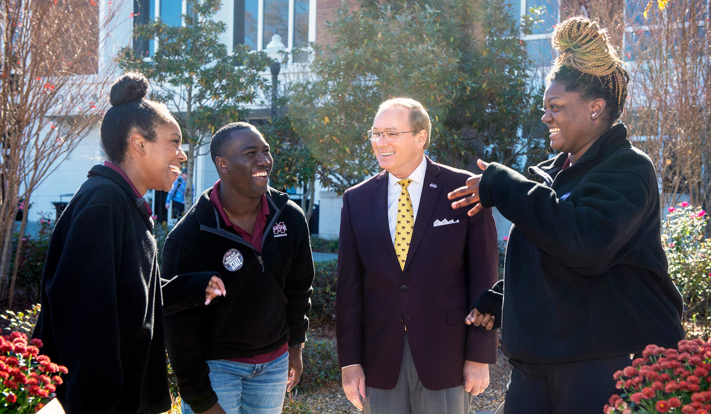 Three students laughing with man in blazer