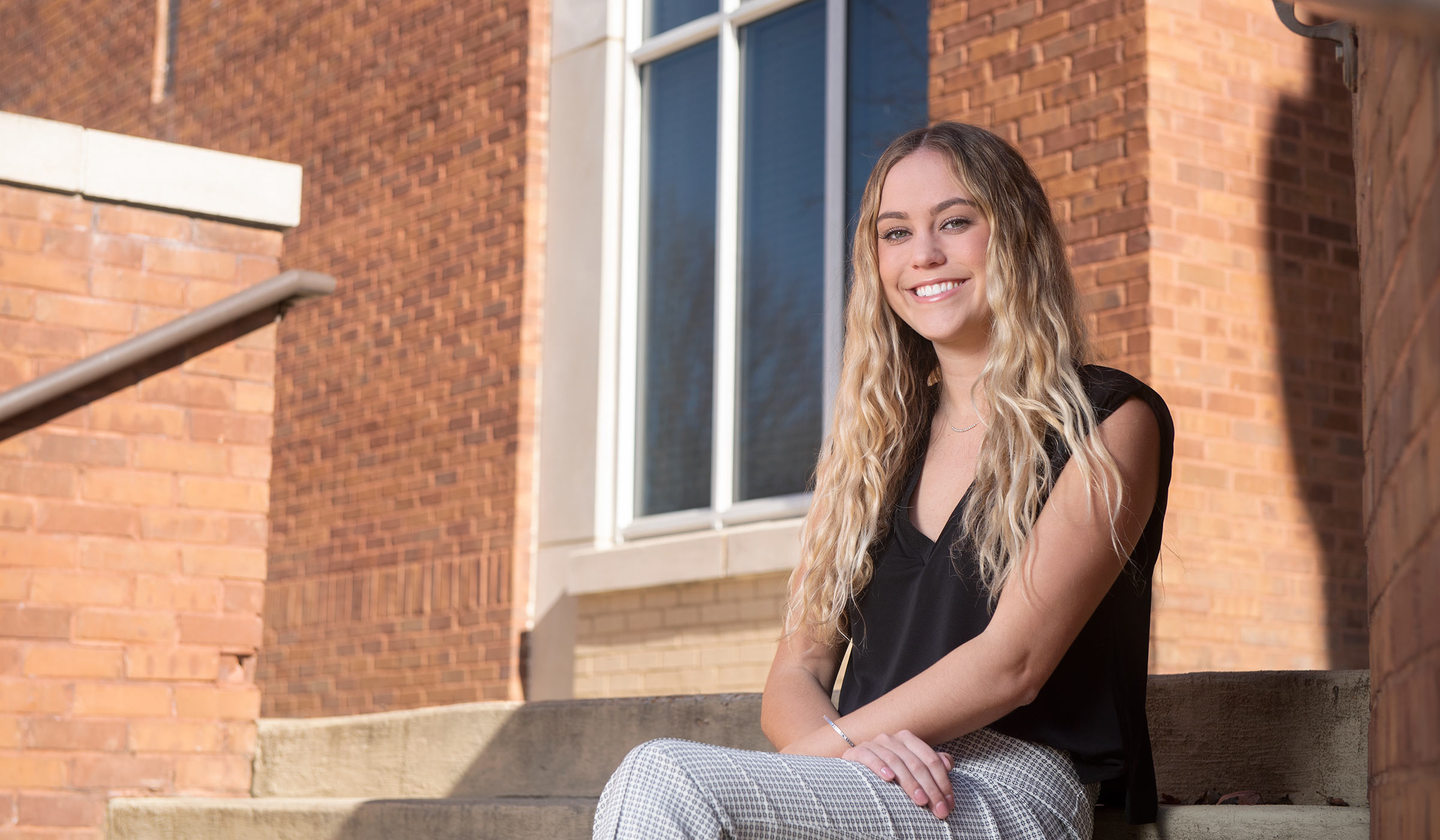 MSU student Allyson Jansen smiles while seated outside on the steps of a campus building.