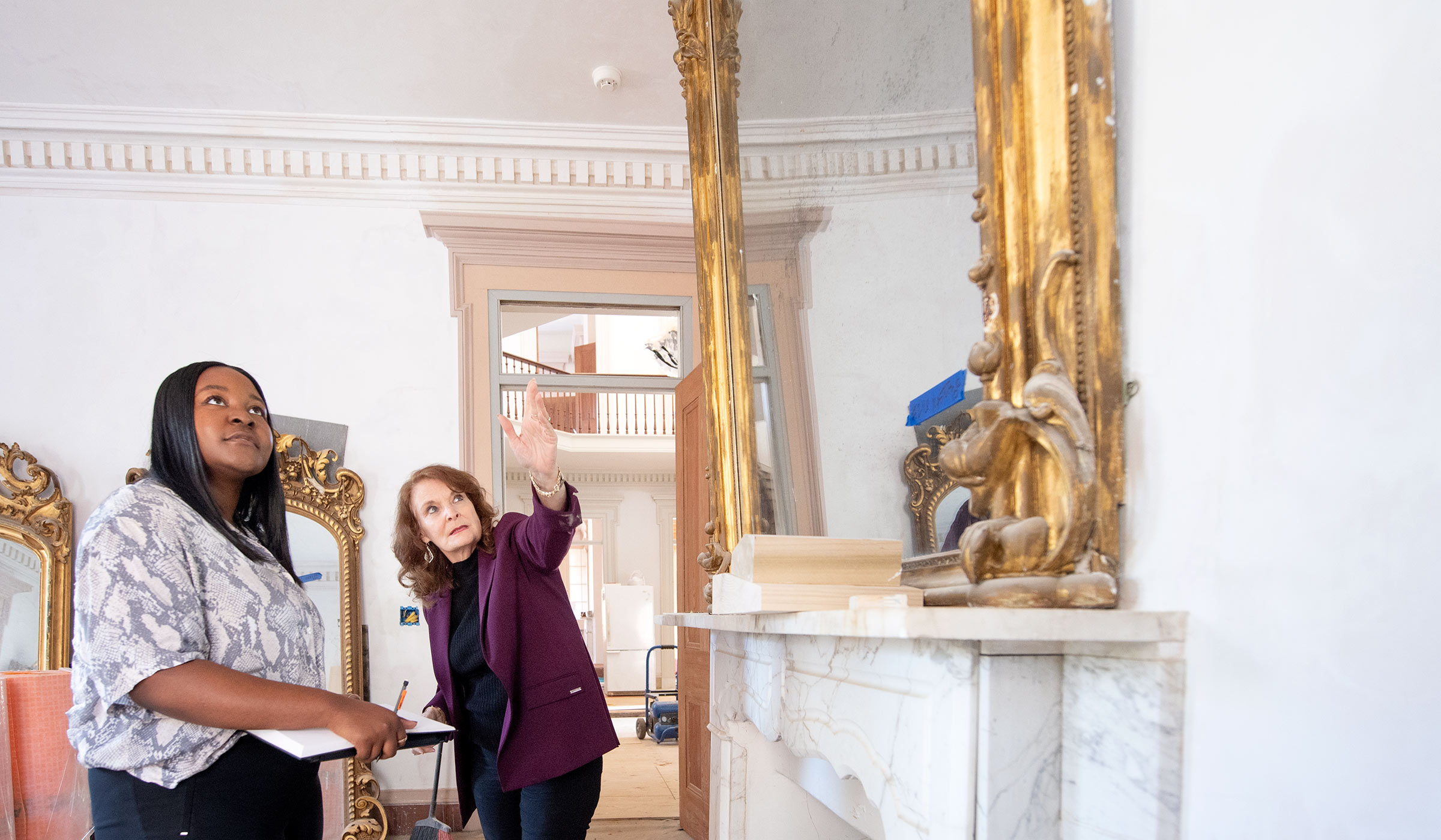 Female student and female professor in a historic house under renovation discussing a vintage mirror and molding