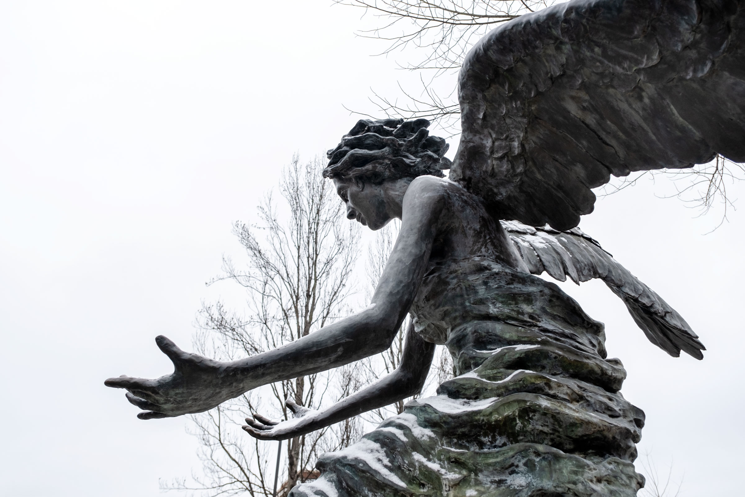 Chapel Angel bronze statue with a light snow dusting and white sky.