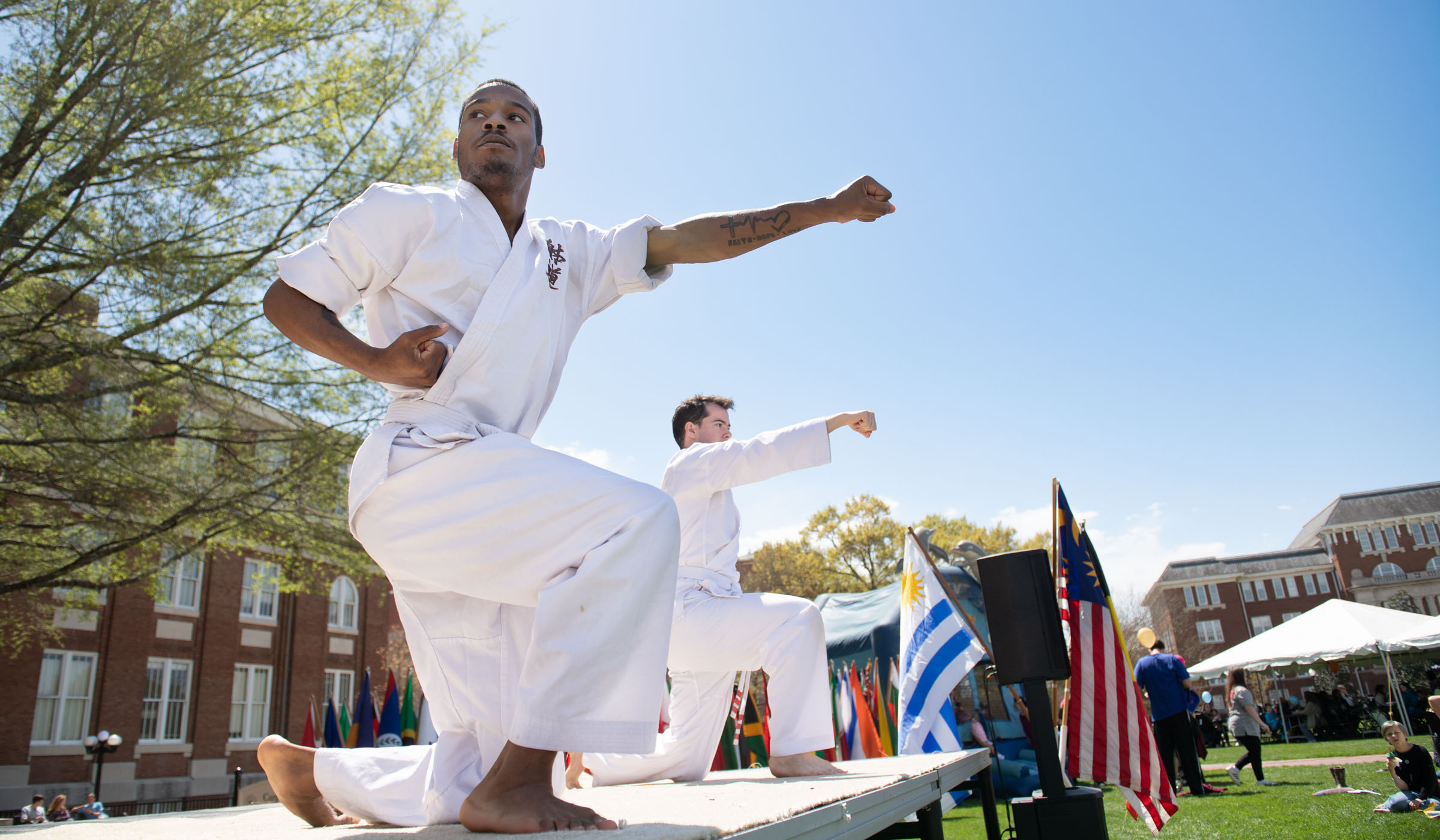 With a blue sky behind them, two MSU Taido Club students wearing all white perform on the International Fiesta stage.