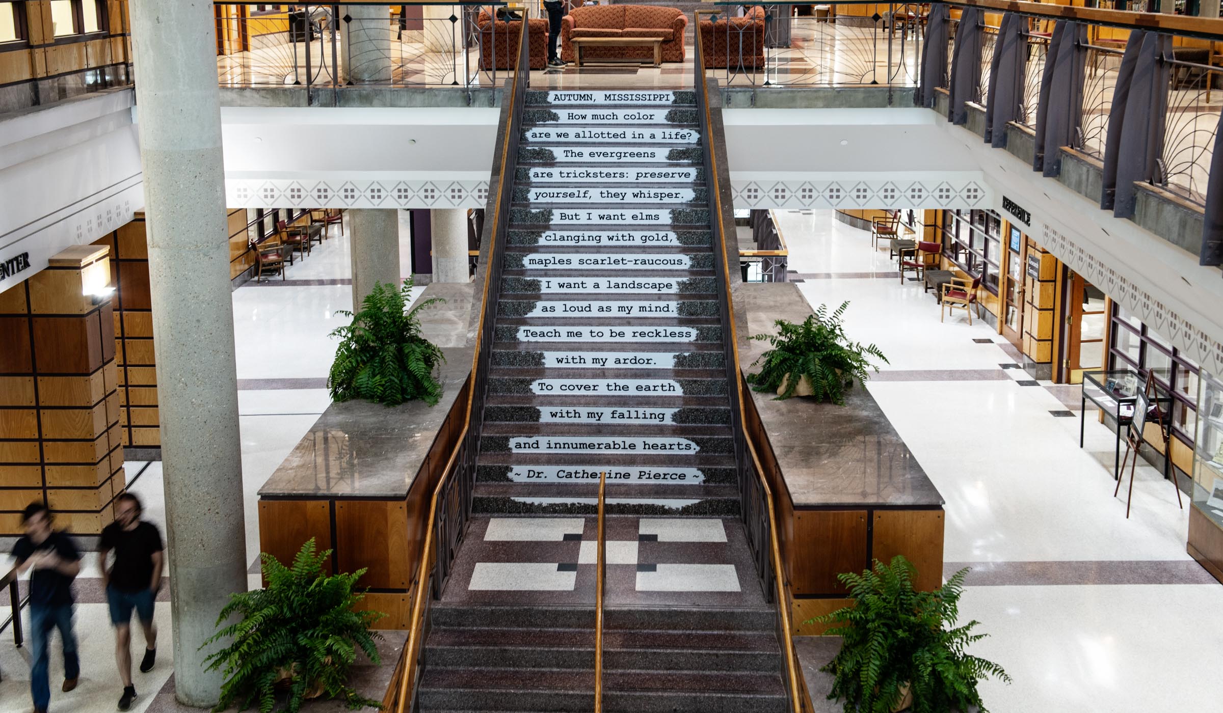 View from the second floor of Mitchell Memorial Library atrium, looking down towards the lobby and the stairs that have a poem by Mississippi Poet Laureate Catherine Pierce running down them.