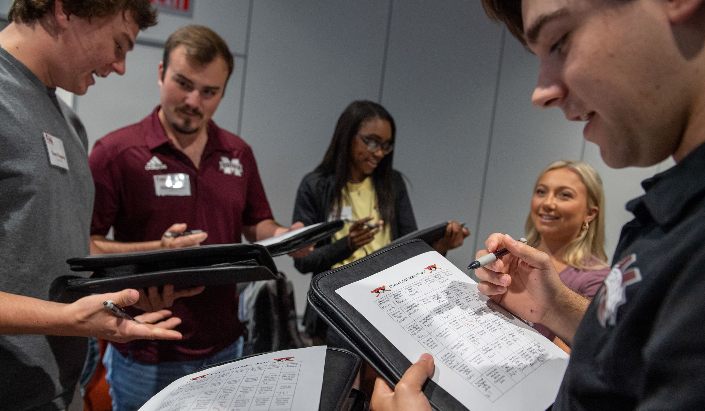 Five MBA students have a lively interaction, each filling out their own MBA student stat &quot;Bingo&quot; sheets with info about eachother.