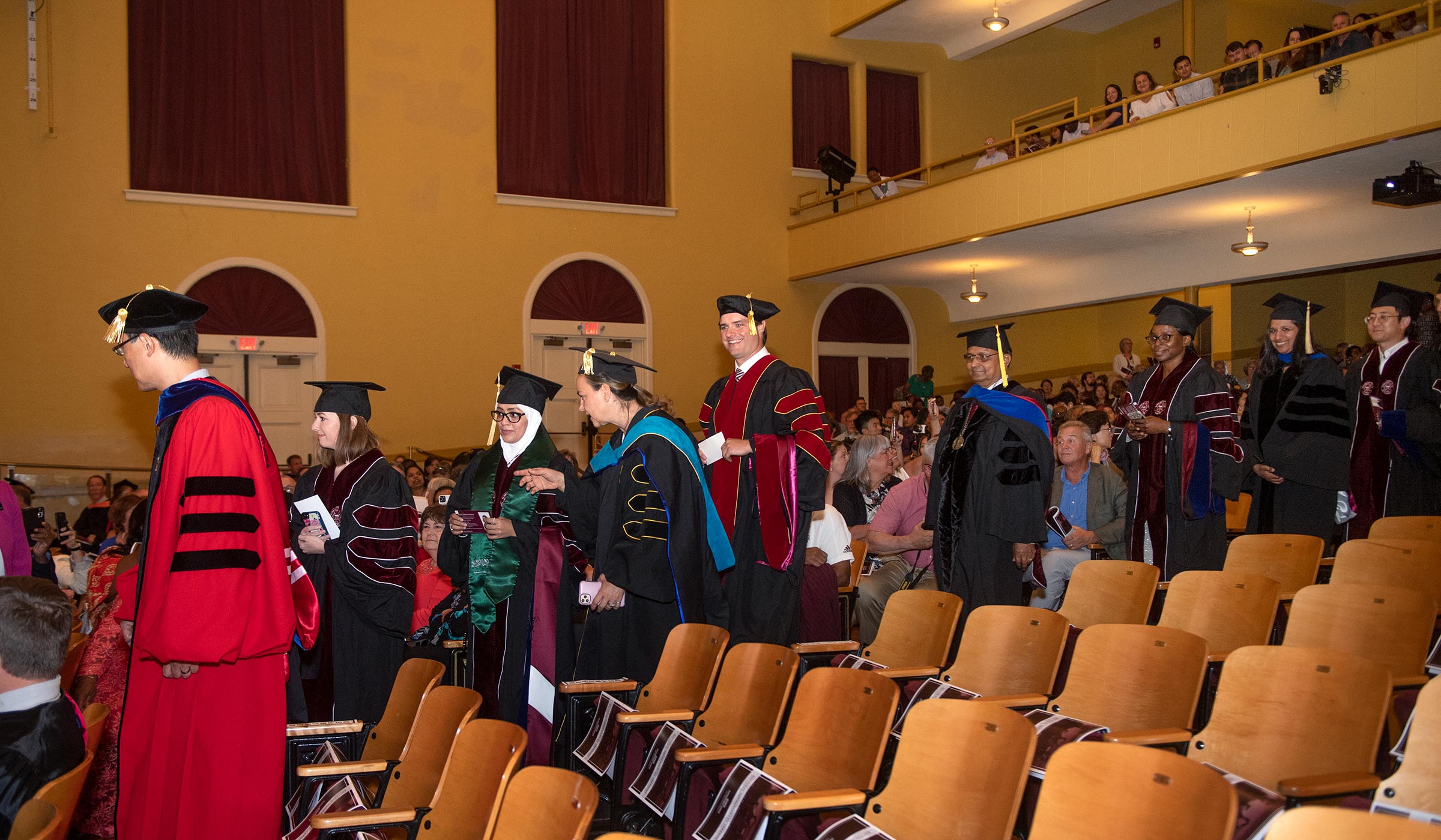 People entering auditorium in graduation regalia smiling