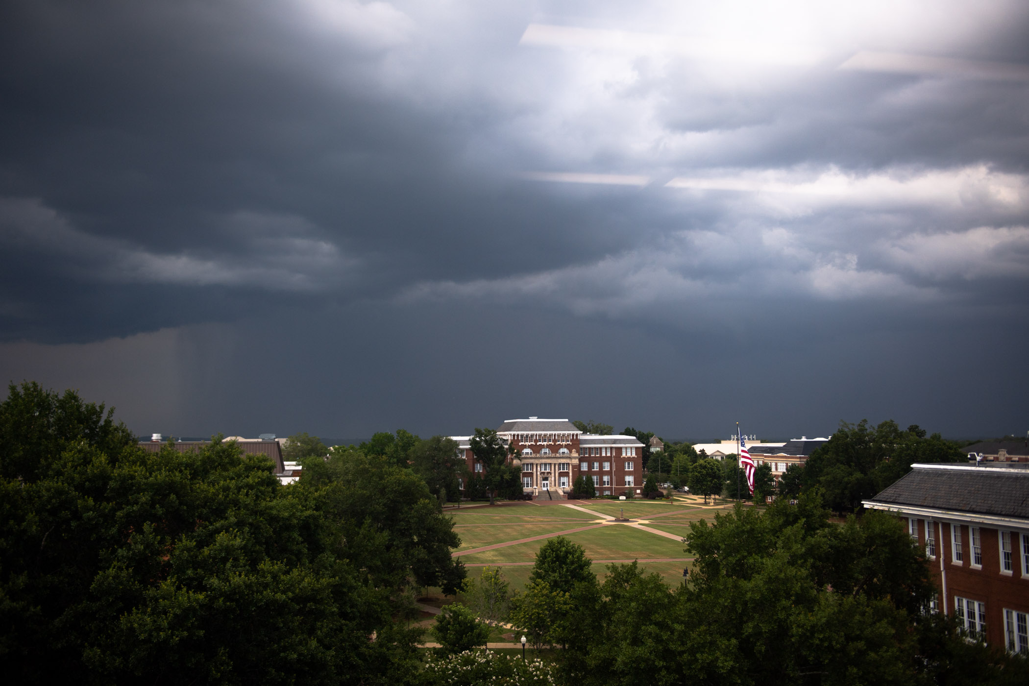 A dark grey sky cascades across MSU&#039;s Drill Field as an incoming summer shower is seen above Lee Hall