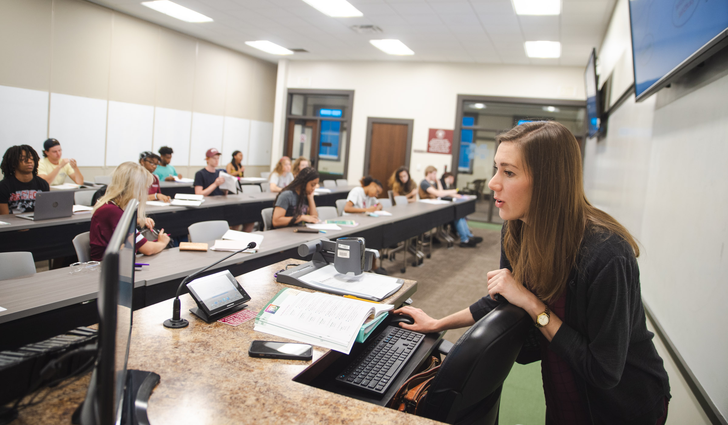 Learning Center Instructor Chelsea Vincent teaches while operating the computer podium, while students take notes in the background of the classroom.