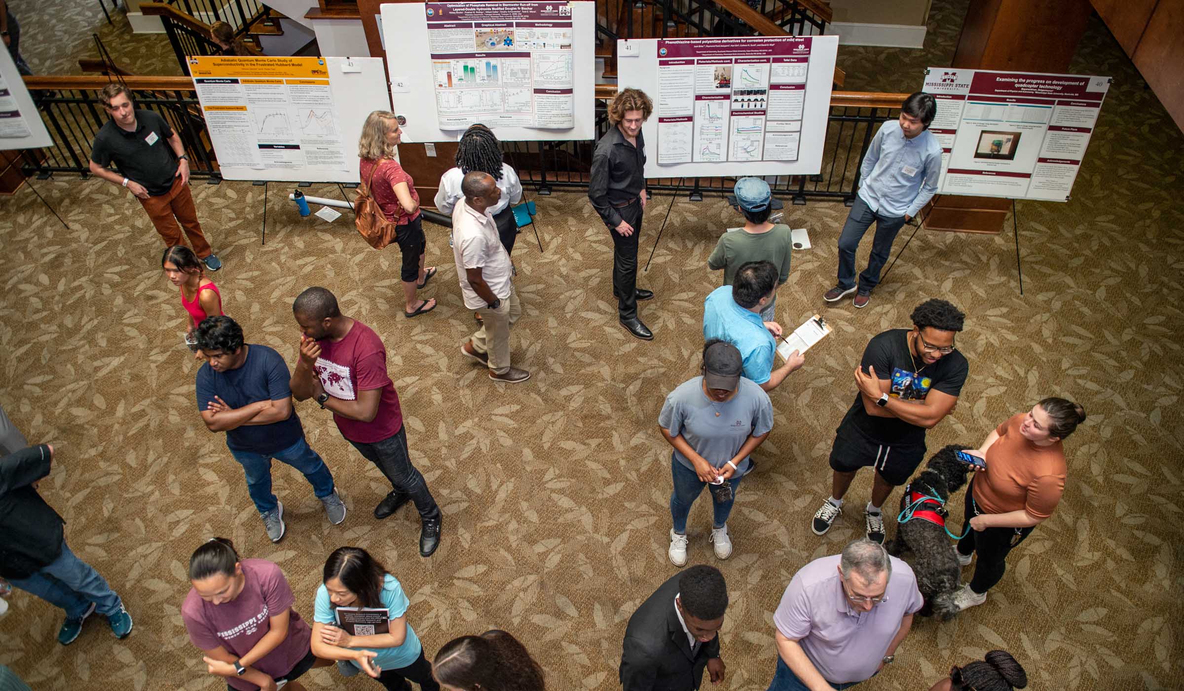 Overhead view looking down at over 20 attendees and presenters talking in front of research posters displayed on the 3rd floor atrium of Griffis Hall.
