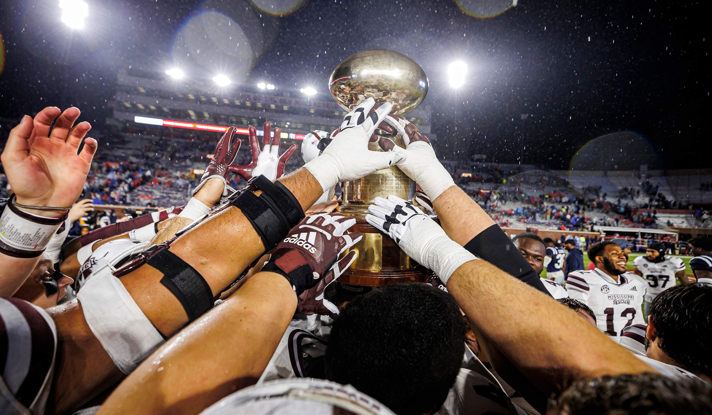 Football players in maroon and white holding a golden egg trophy above their heads as a team