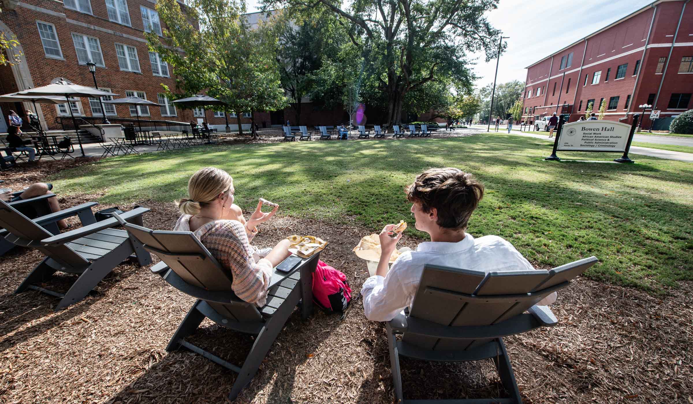 Two students sit in Adirondack chairs in the sunshine outside Bowen Hall.