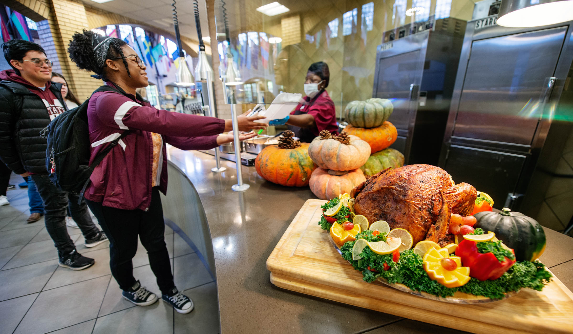 Students line up in the Thanksgiving food line at Perry, with a full roasted turkey in the right foreground.