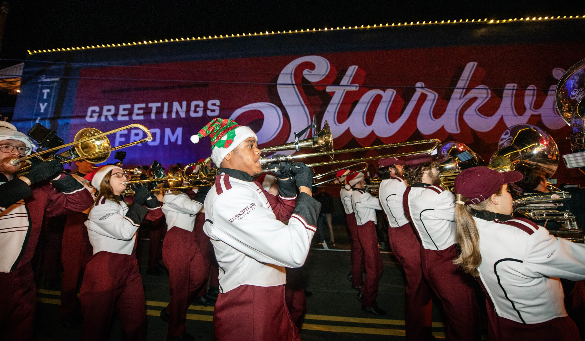 Members of MSU&#039;s Famous Maroon Marching Band march past the &quot;Greetings From Starkville&quot; mural during the Christmas parade.