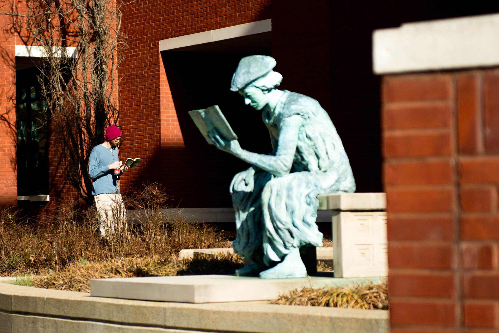 Passerby and MSU Libraries&#039; favorite statue, &quot;The Scholar,&quot; enjoy their books on a sunny afternoon.
