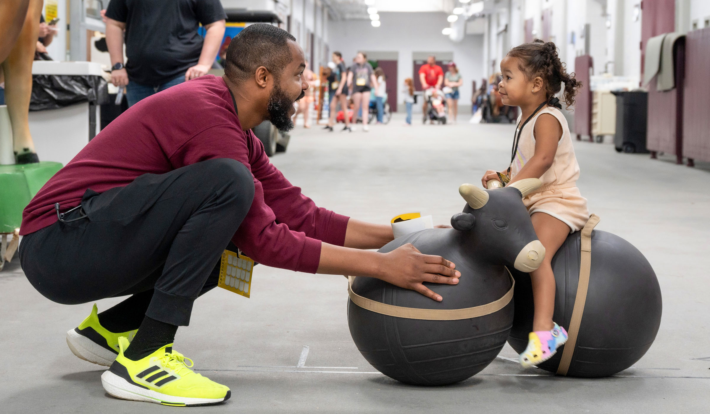 CVM student Matthew Tennin (af left) crouches on the ground to play with his daugher, with his daughter on a cow-shaped bouncy ball inside the Wise Center.