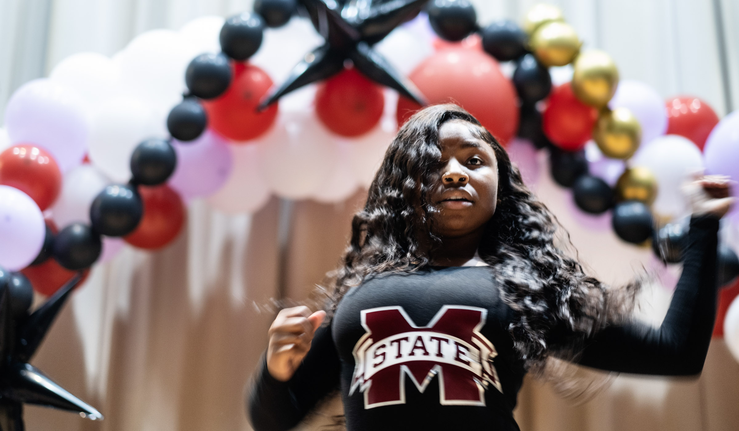 Wearing a long sleeved black unitard with an MState logo in the middle, Breanna Spencer, performs her &quot;hip-hop majorette&quot; performance with an arch of balloons against the stage curtain behind her.