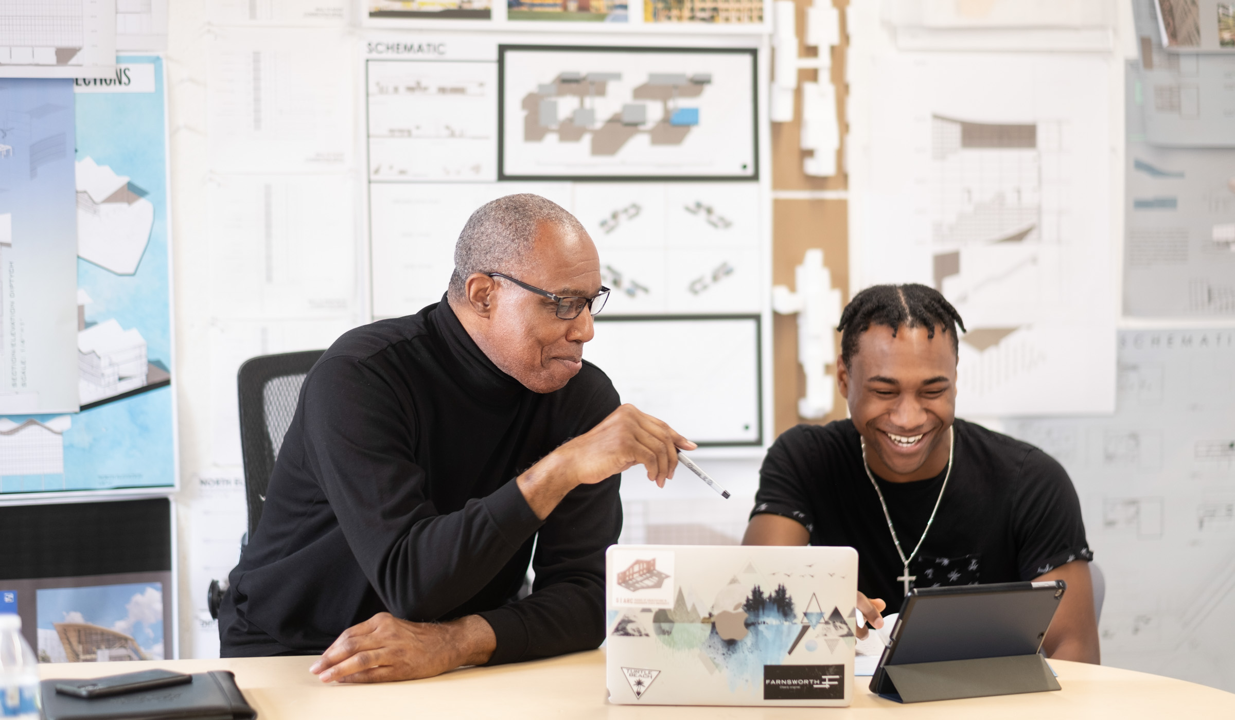 With architectural drawings on the wall behind them, Professor Hunter (L) points with a pen at student Alston Brown&#039;s computer screen.