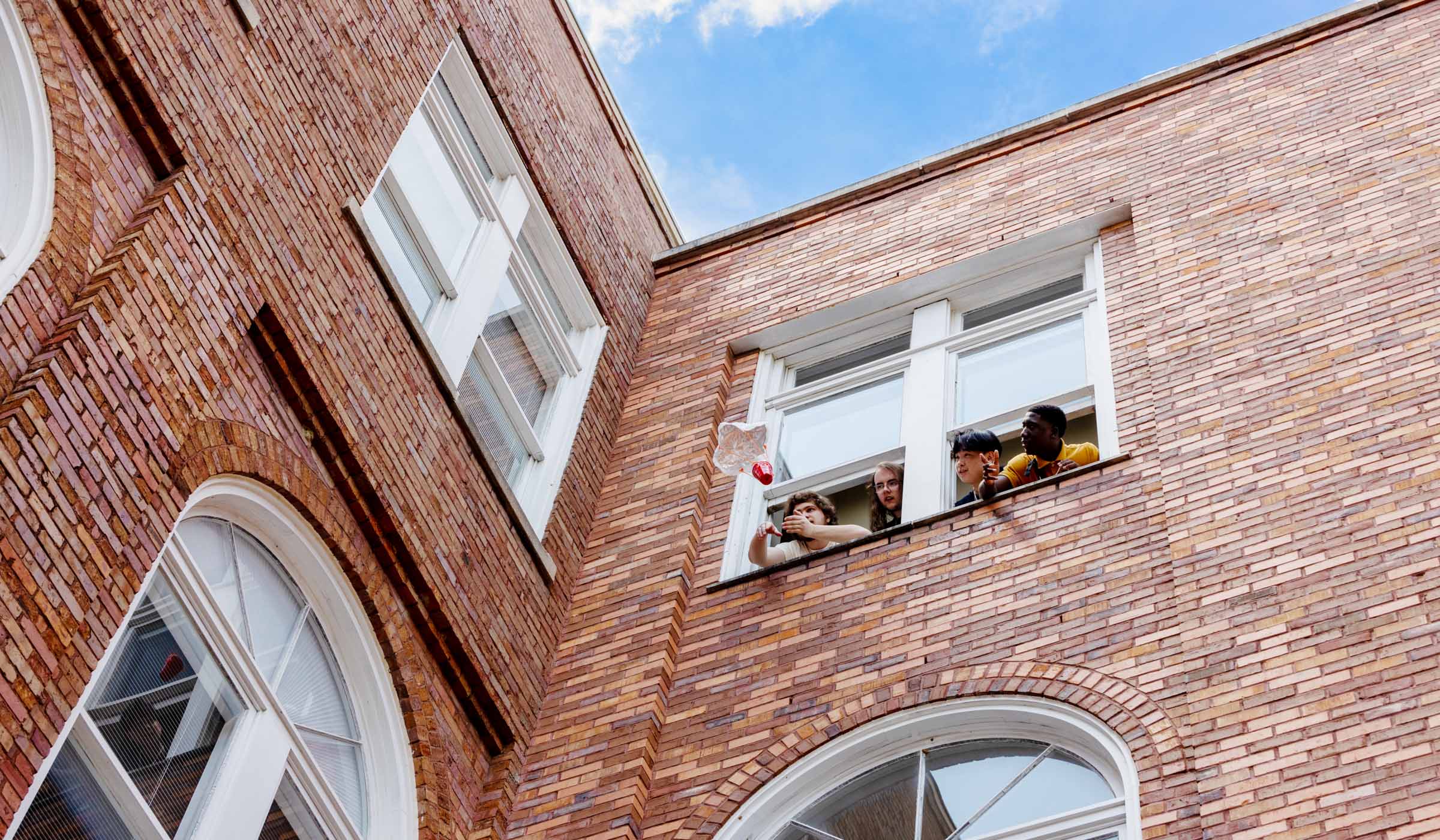 Four teen Engineering Camp participants stick their head out of an upper exterior window at McCain Hall to release an egg with a parachute attached.