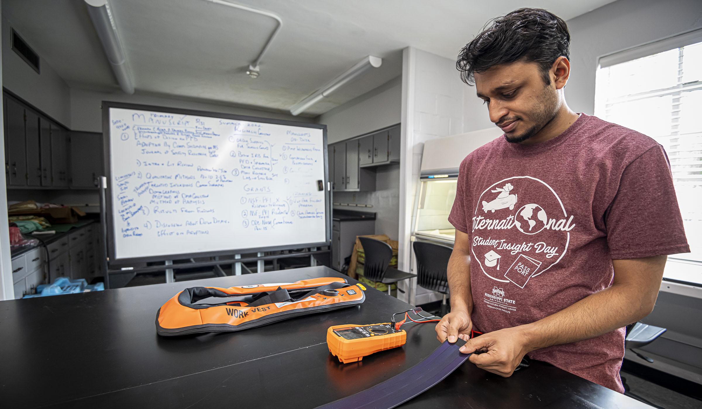 Graduate student Amit Talukder works on the solar panels for the orange life vest prototype stretched out next to him on the lab&#039;s black table.