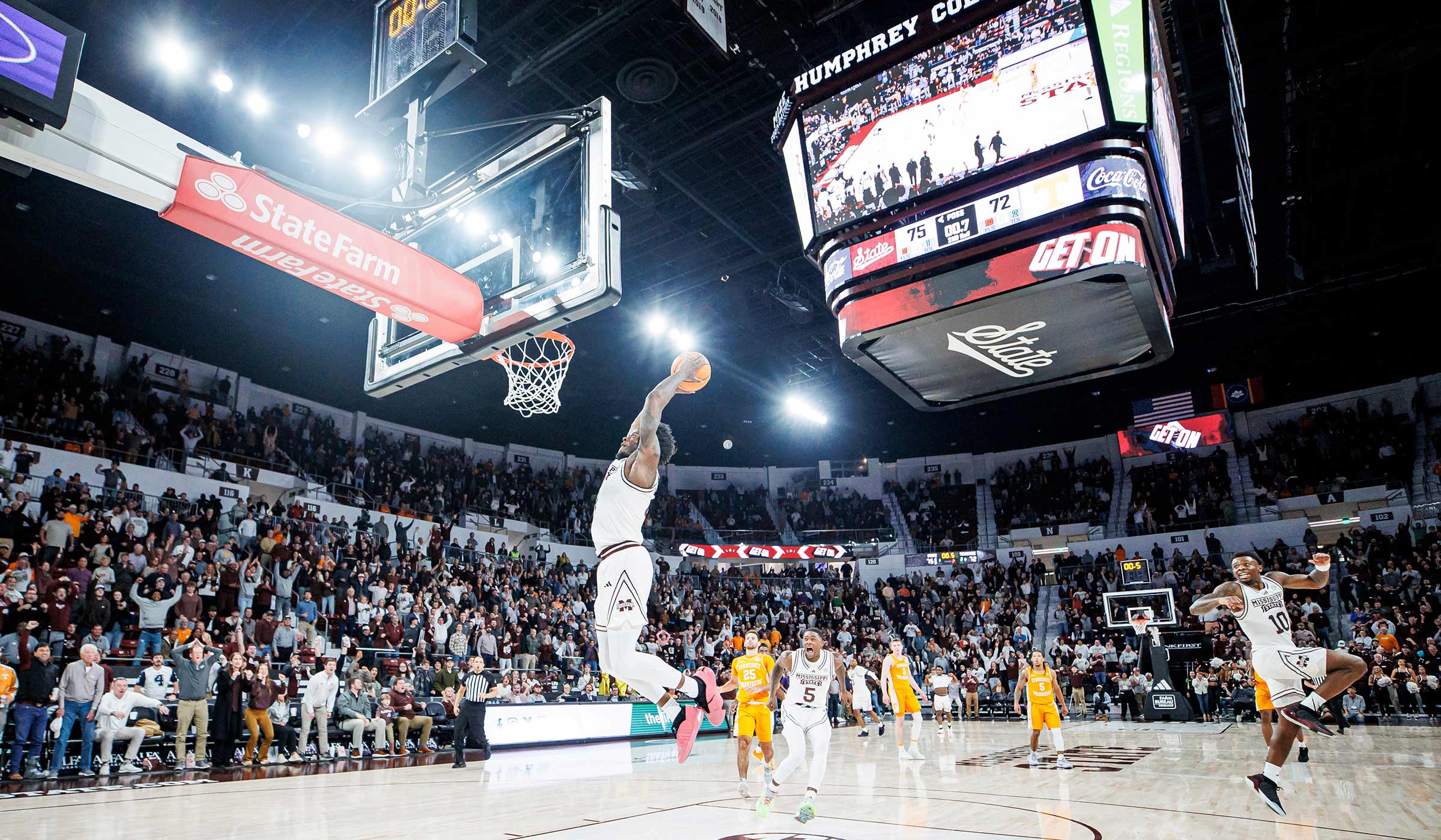 Basketball player in white going for dunk on basket with ball with fans excited in background