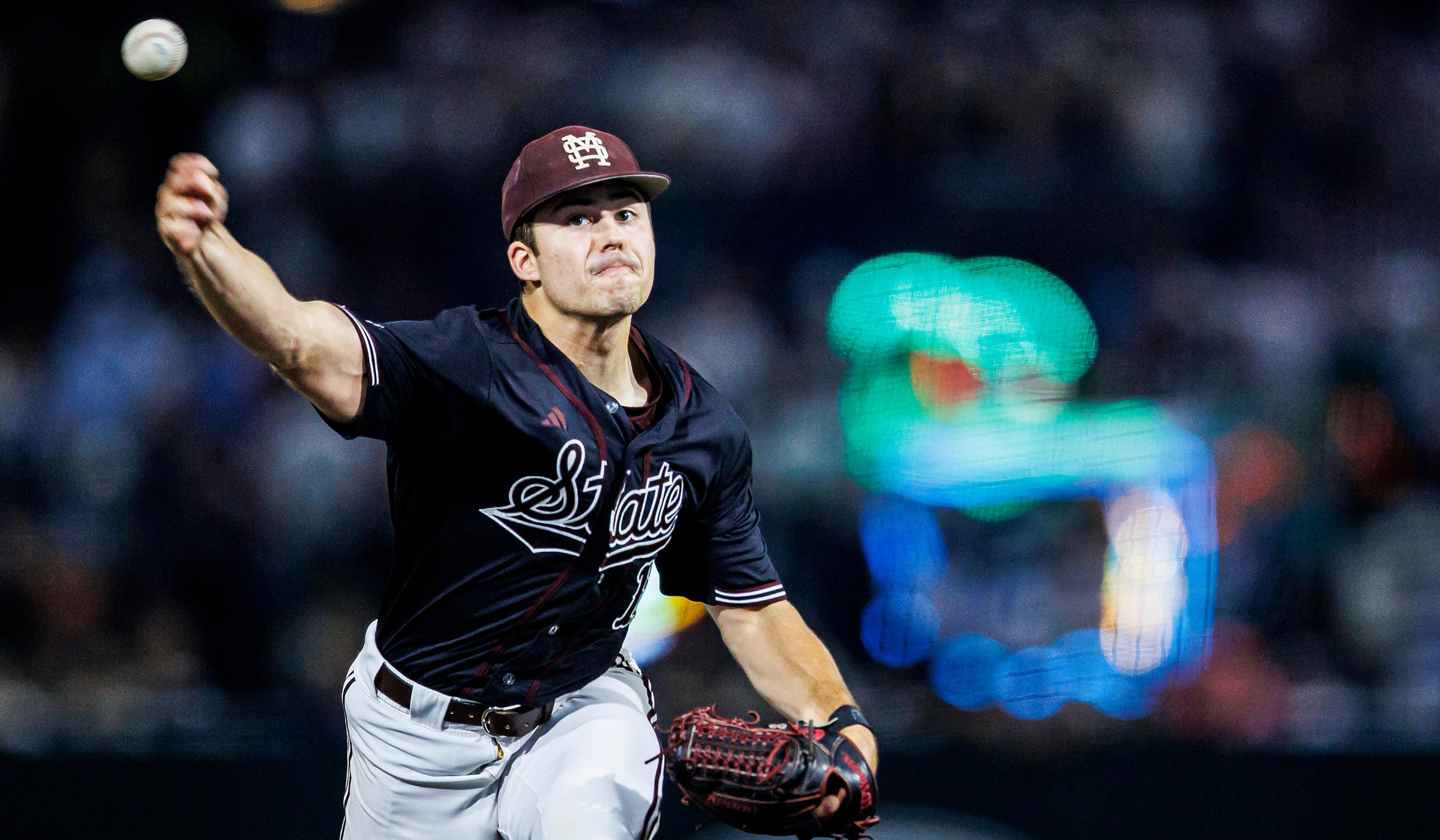 Pitcher throwing ball wearing black and maroon jersey and maroon cap