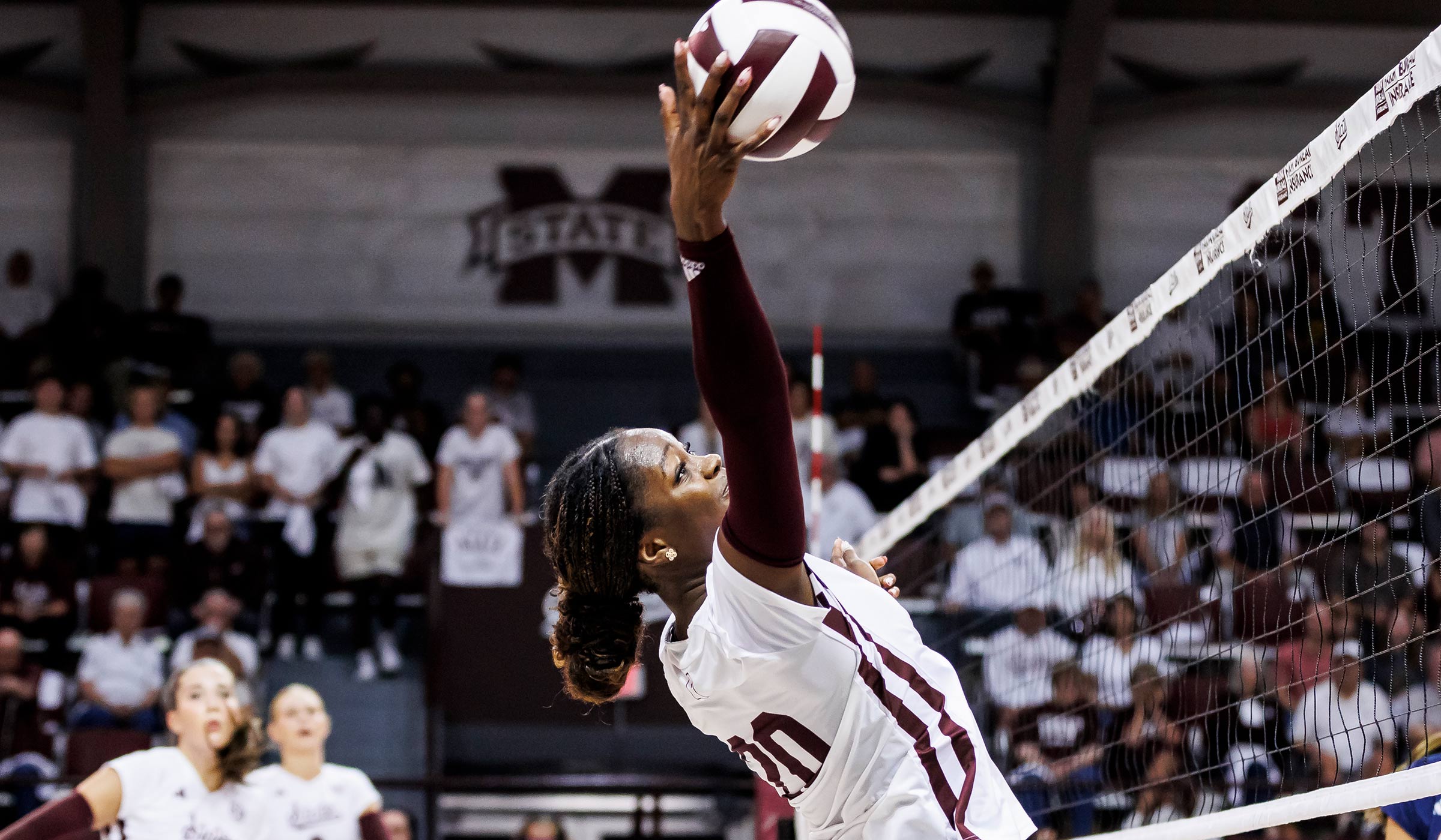 Volleyball player in maroon and white jumping to strike ball at net