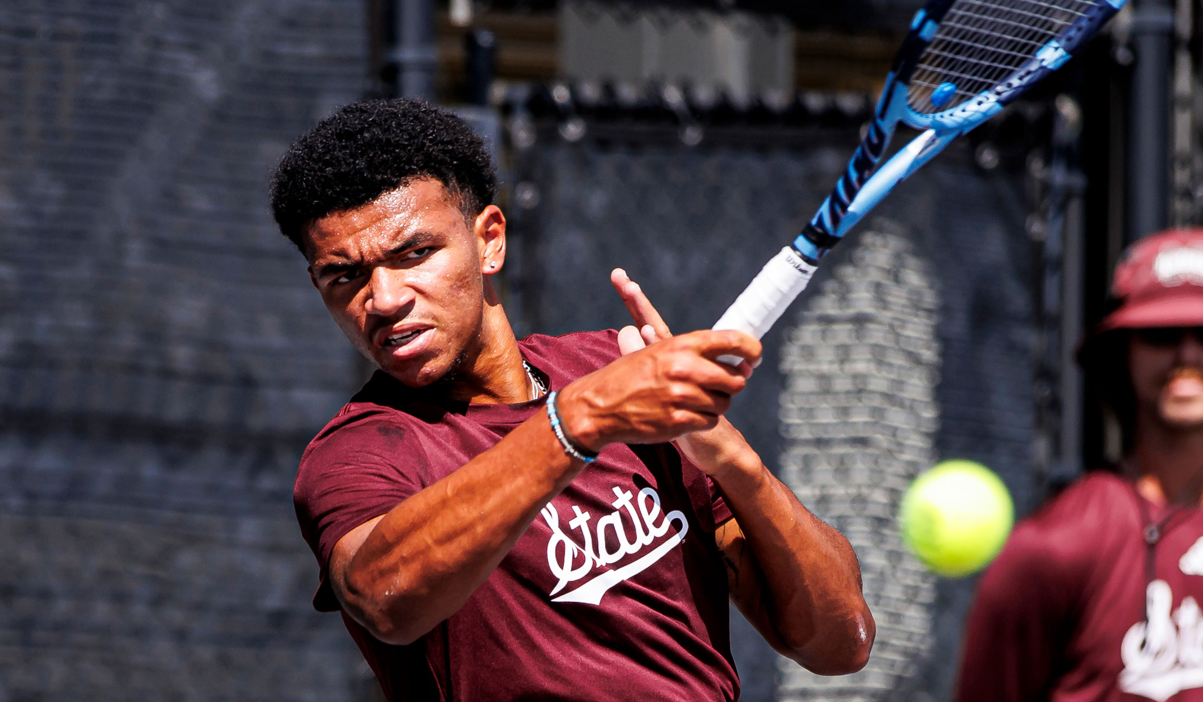 Tennis player in maroon shirt striking the ball with a forehand hit.