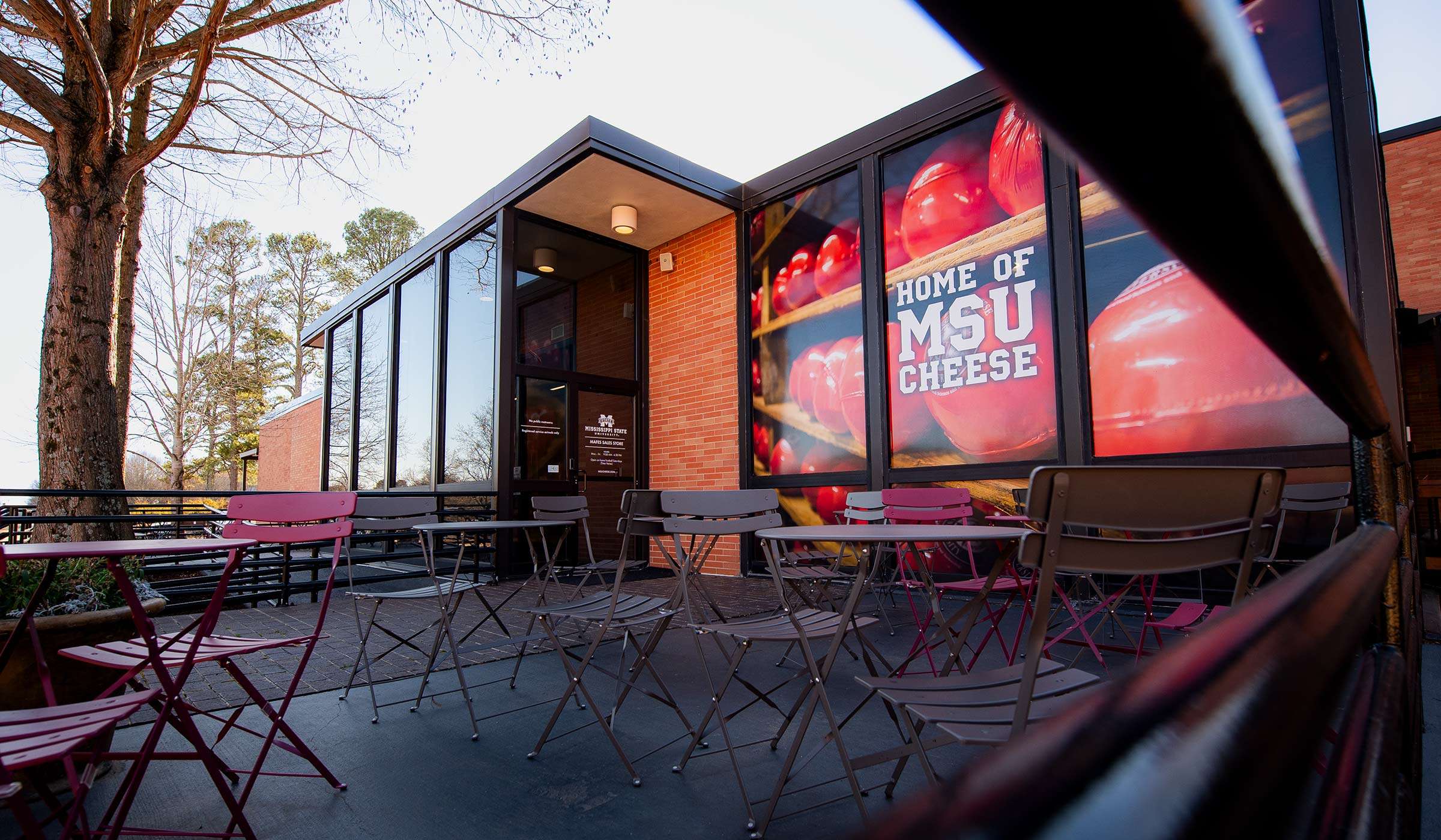 Glass and brick building with large wrapped cheese balls with patio furniture and railing in foreground