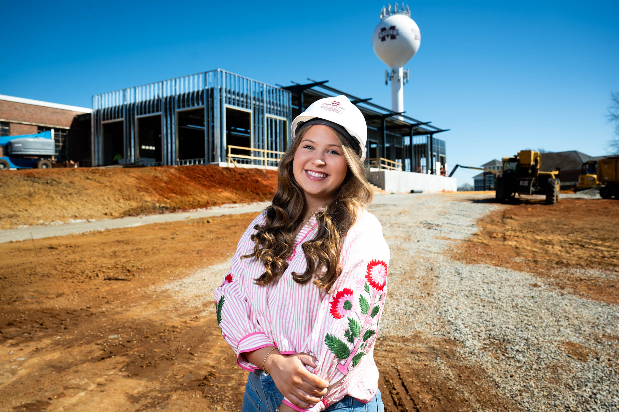 a young woman wearing a construction hat in front of a building site