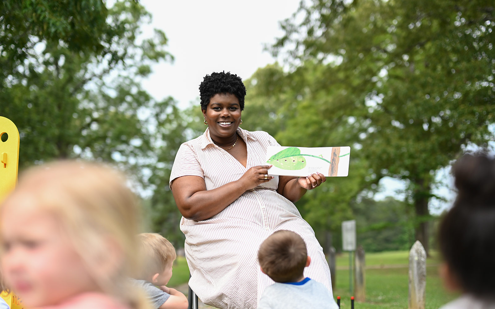 a woman reading a book to children outside