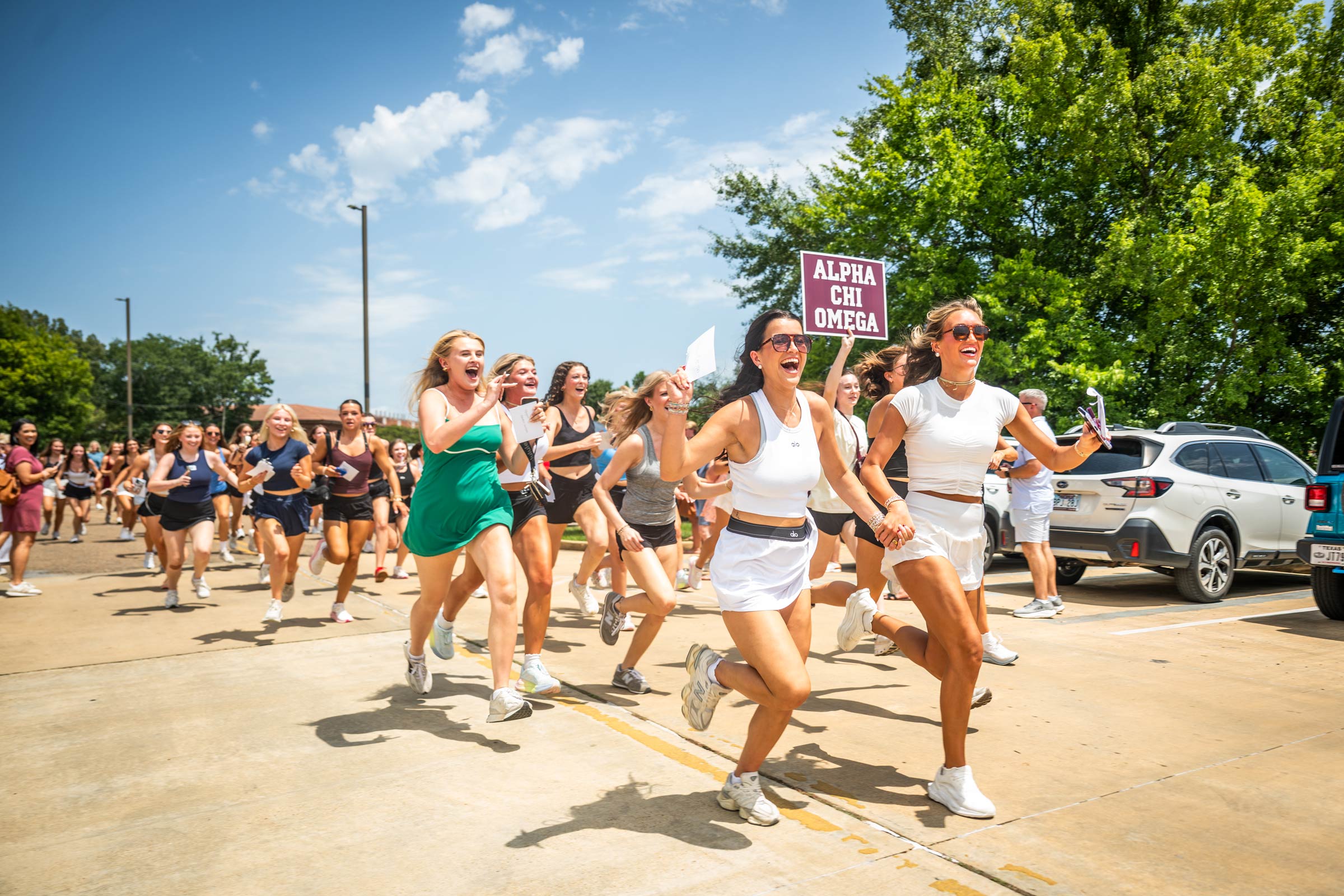 A large group of girls happily scream and run across campus to their Greek organizations