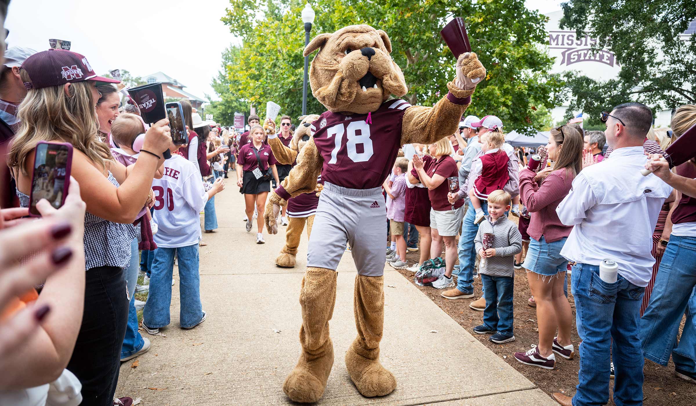 Mascot Bully, in a maroon jersey, walks through the Dawg Walk while ringing a maroon cowbell.